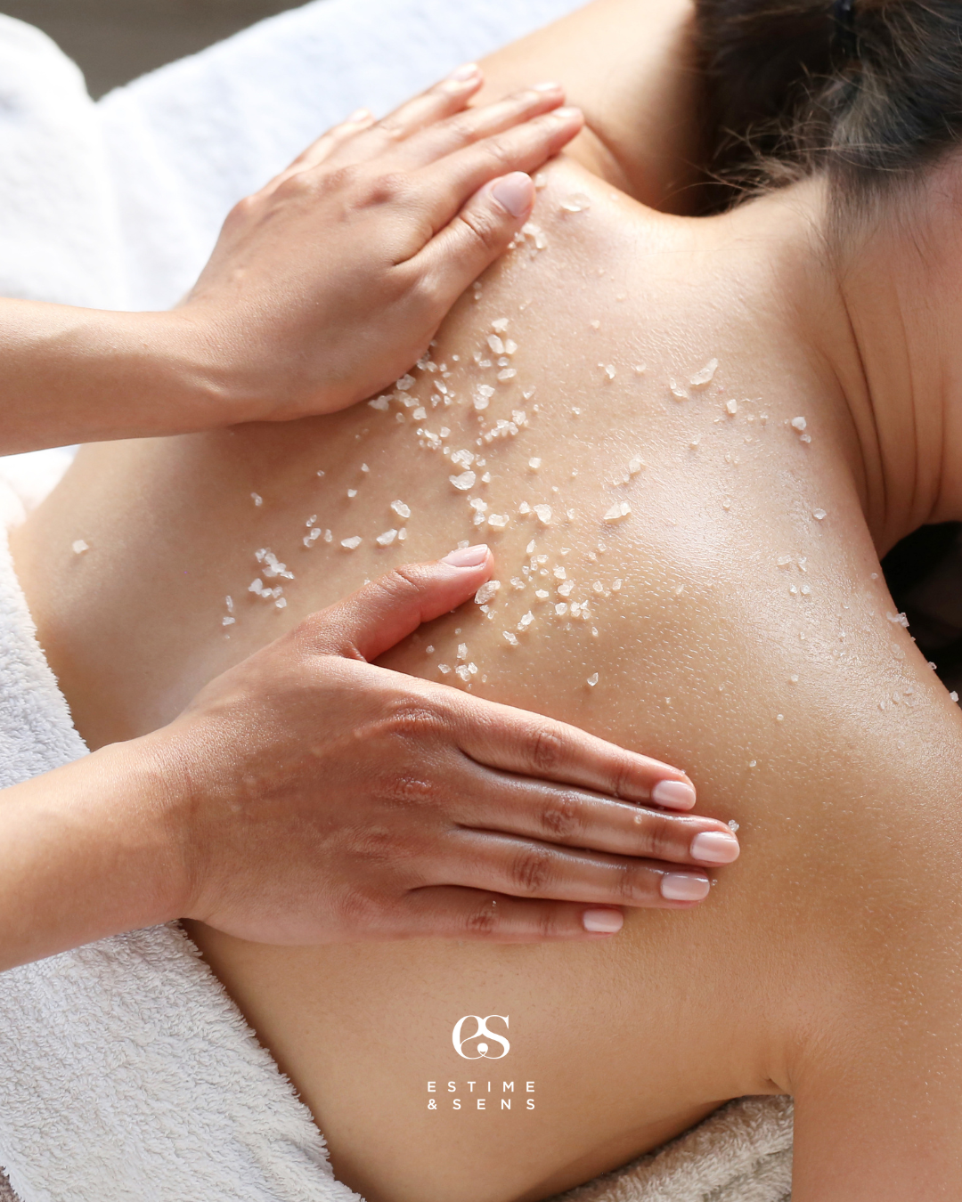 Une personne reçoit un massage avec des sels de massage sur le dos, allongée en position face pour un soin relaxant.