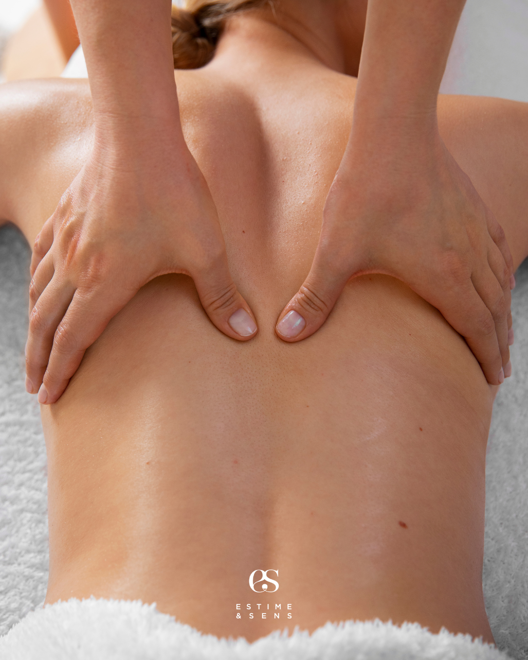 Une personne recevant un massage du dos, allongée sur un lit, avec deux mains appliquant une pression sur la peau nue.