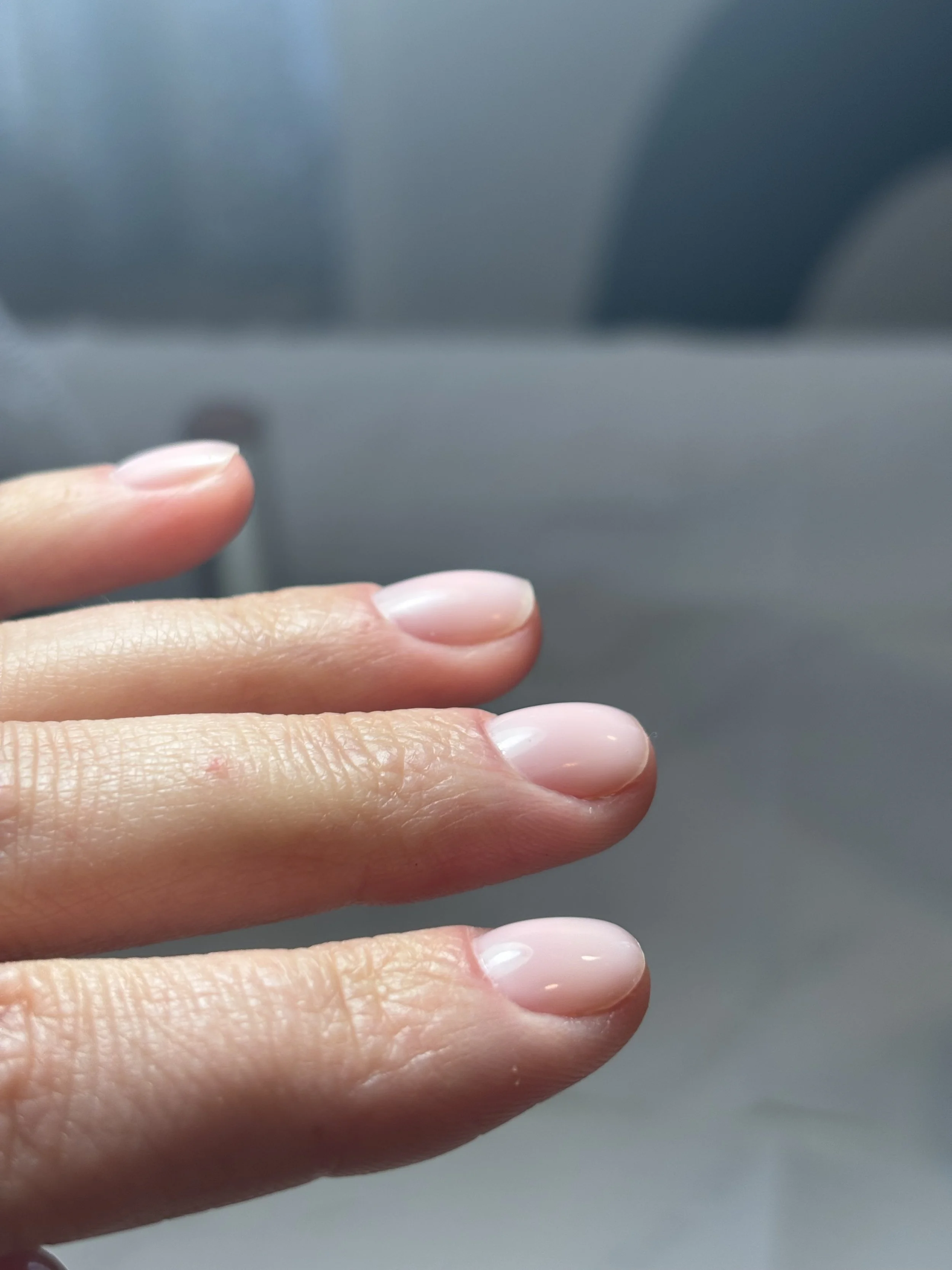 Une main avec des ongles soignés, tenant un objet non visible en arrière-plan.