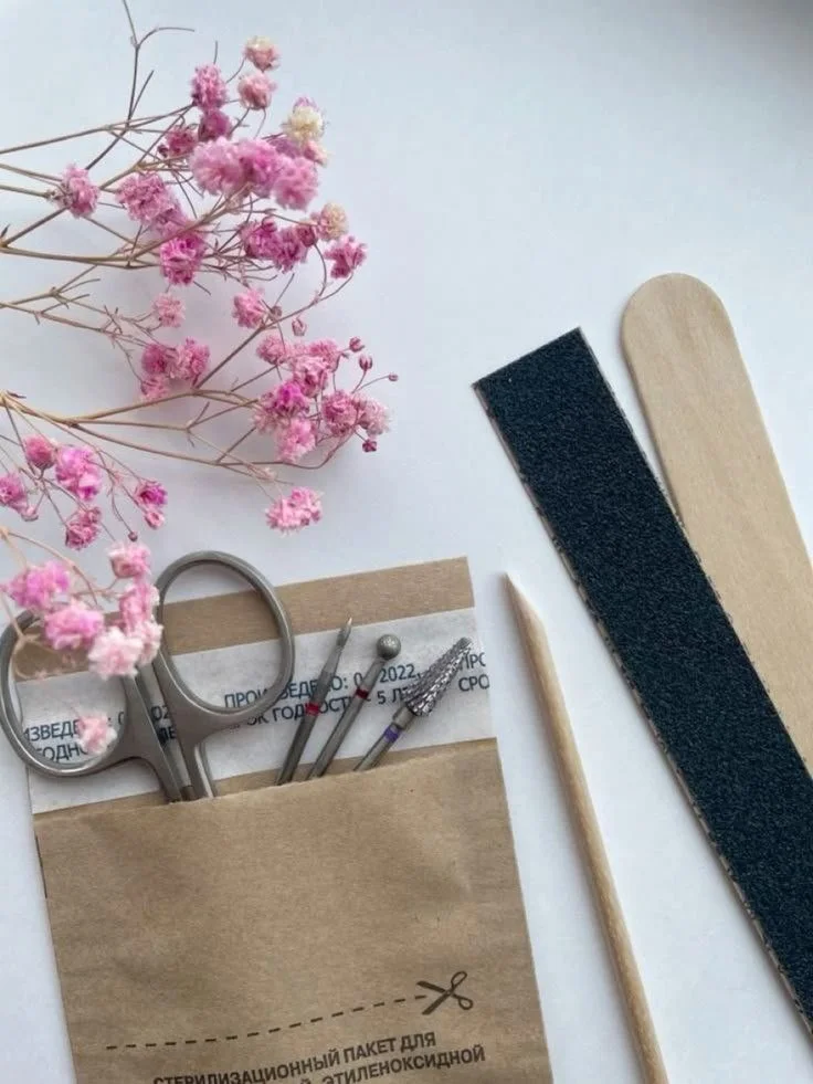 Des fleurs de gypsophile roses, une lime à ongles, une pince à épiler, une brosse en bois, une lime en bois et une fine baguette en bois sur une surface blanche.