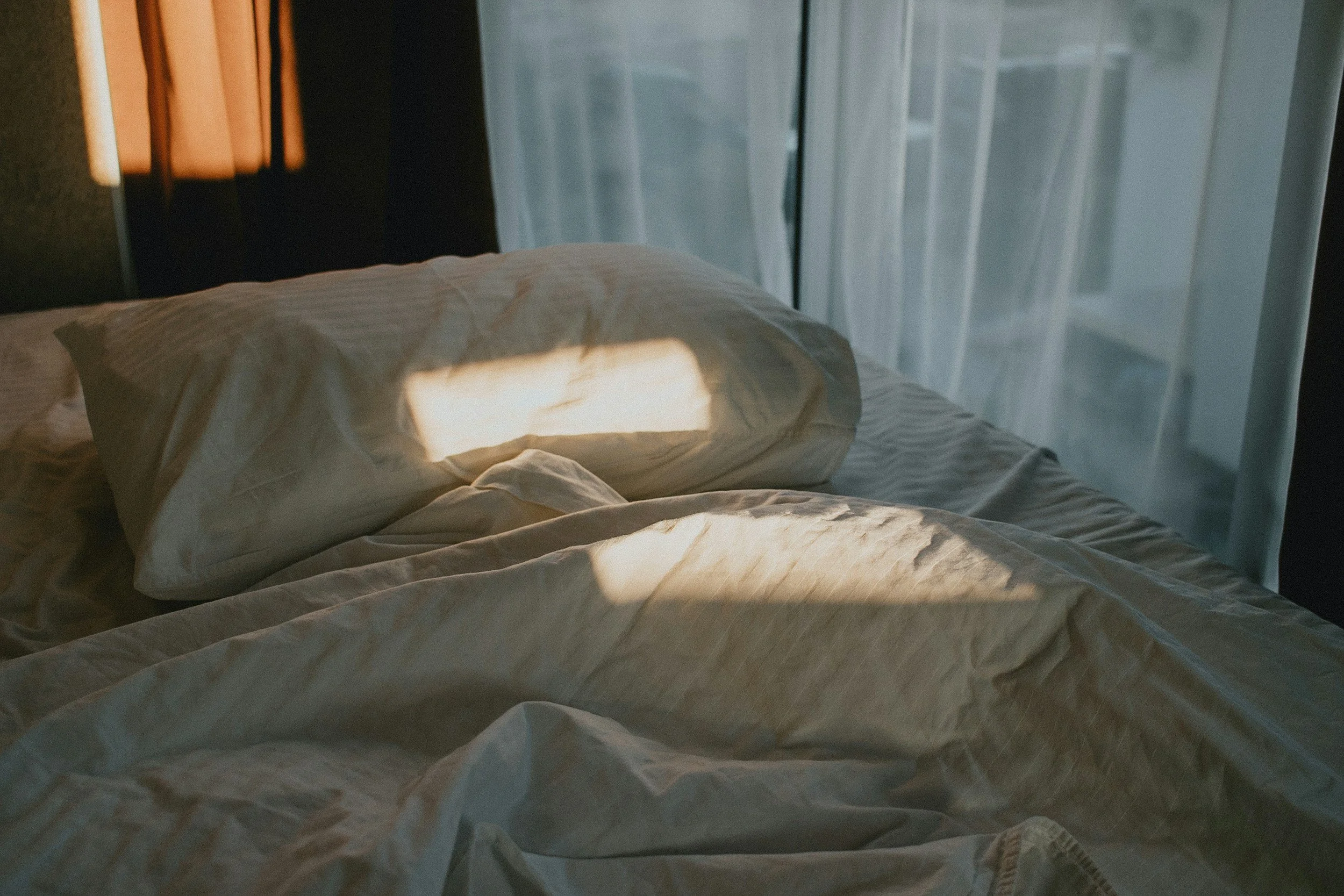 Image of a bed with light hitting the covers, meant to symbolize waking up after experiencing a migraine and entering the postdrome phase or migraine hangover