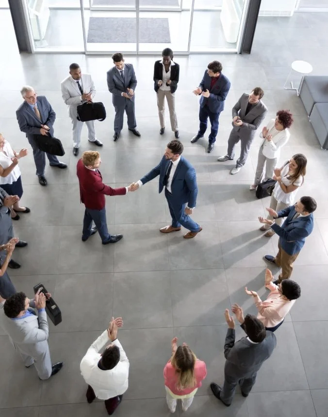 Homens e mulheres de negócios em reunião de assinatura de contrato ou celebração de parceria, com duas pessoas se cumprimentando no centro, formando um coração com as mãos, em um espaço moderno de escritório.