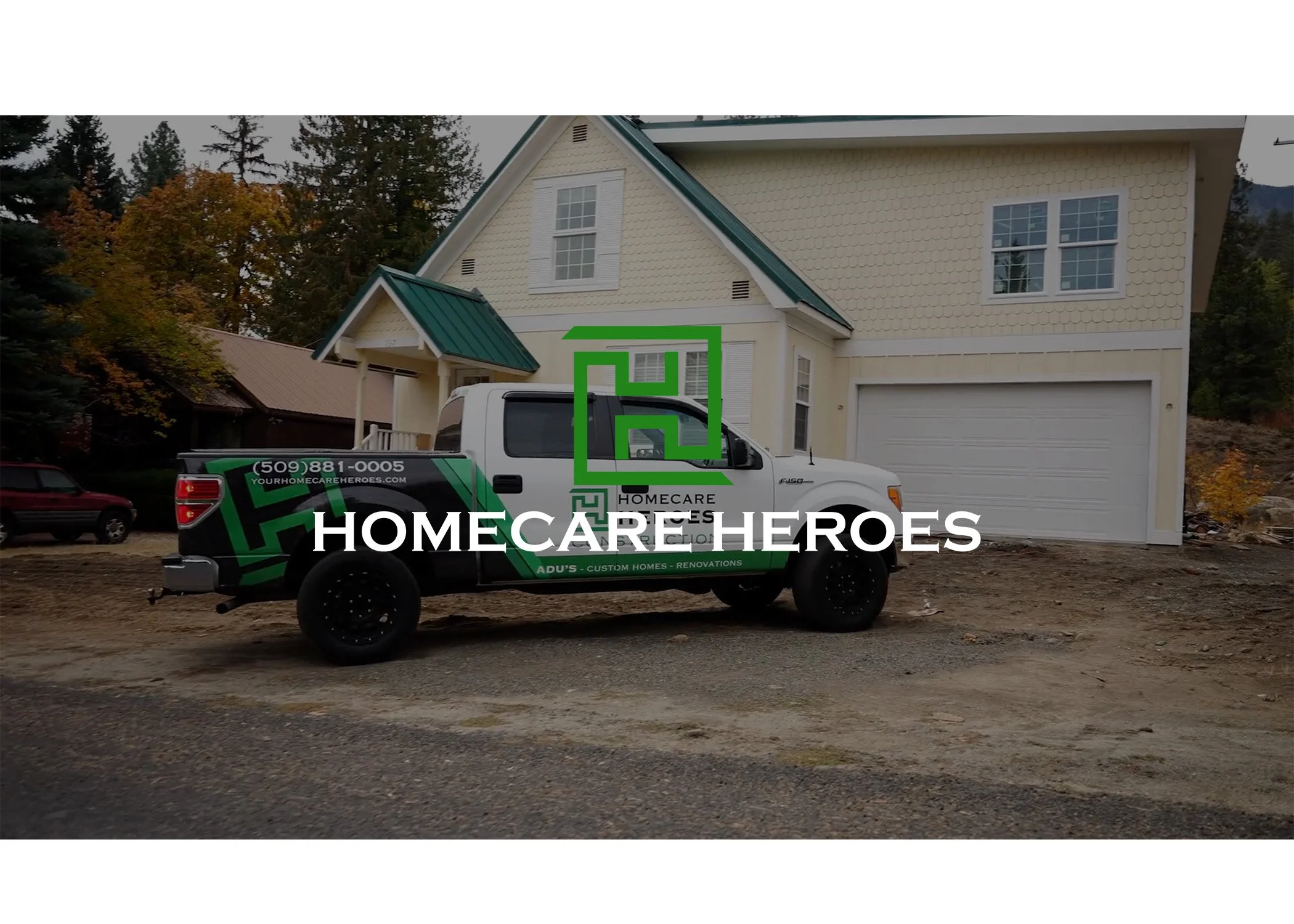 A white home with a green roof and a two-car garage, has a black and green pickup truck parked in front. The truck has the logo and contact information for 'Homecare Heroes', a home renovation company.
