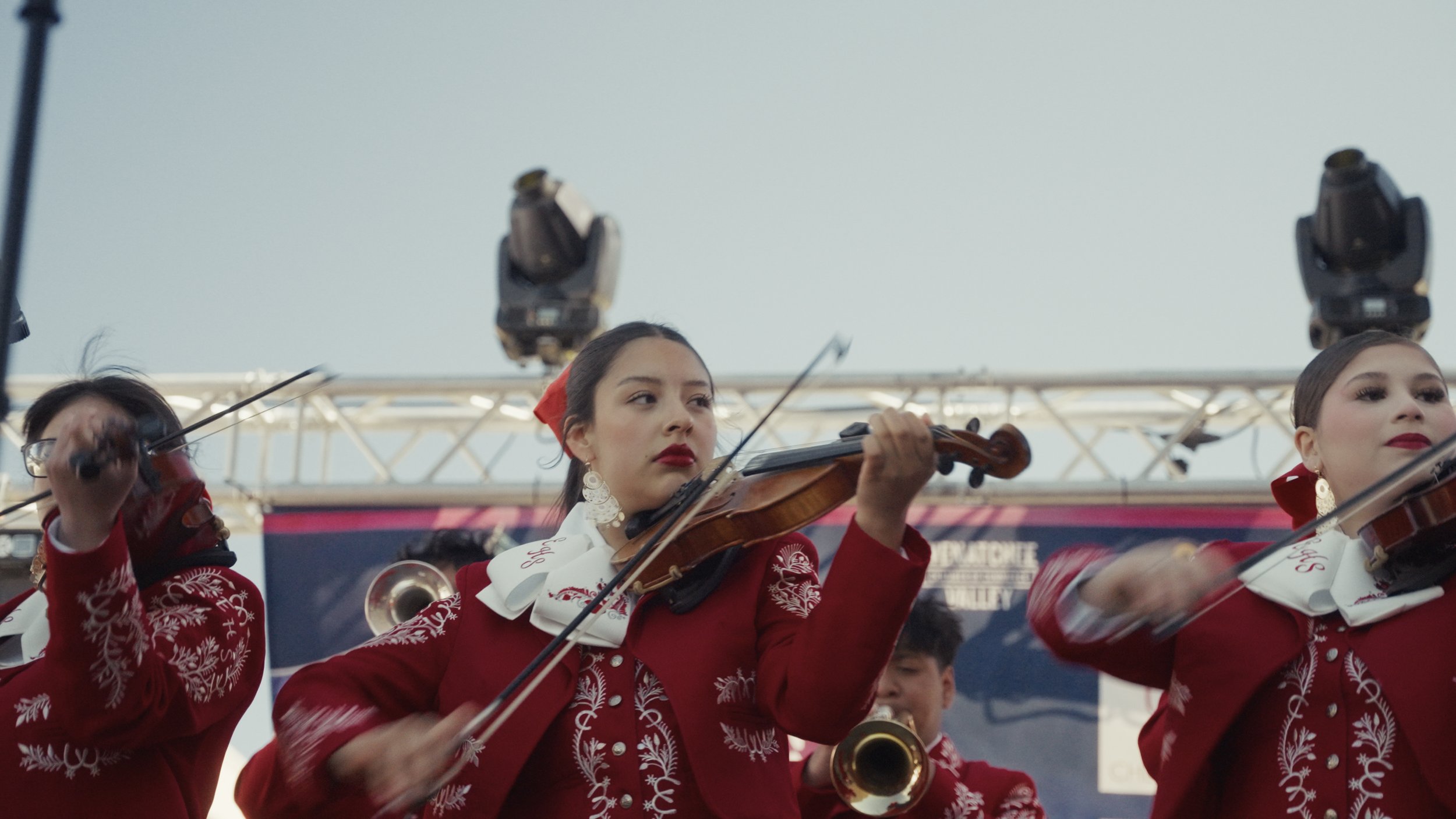Women in red festive outfits playing violins during a holiday performance.