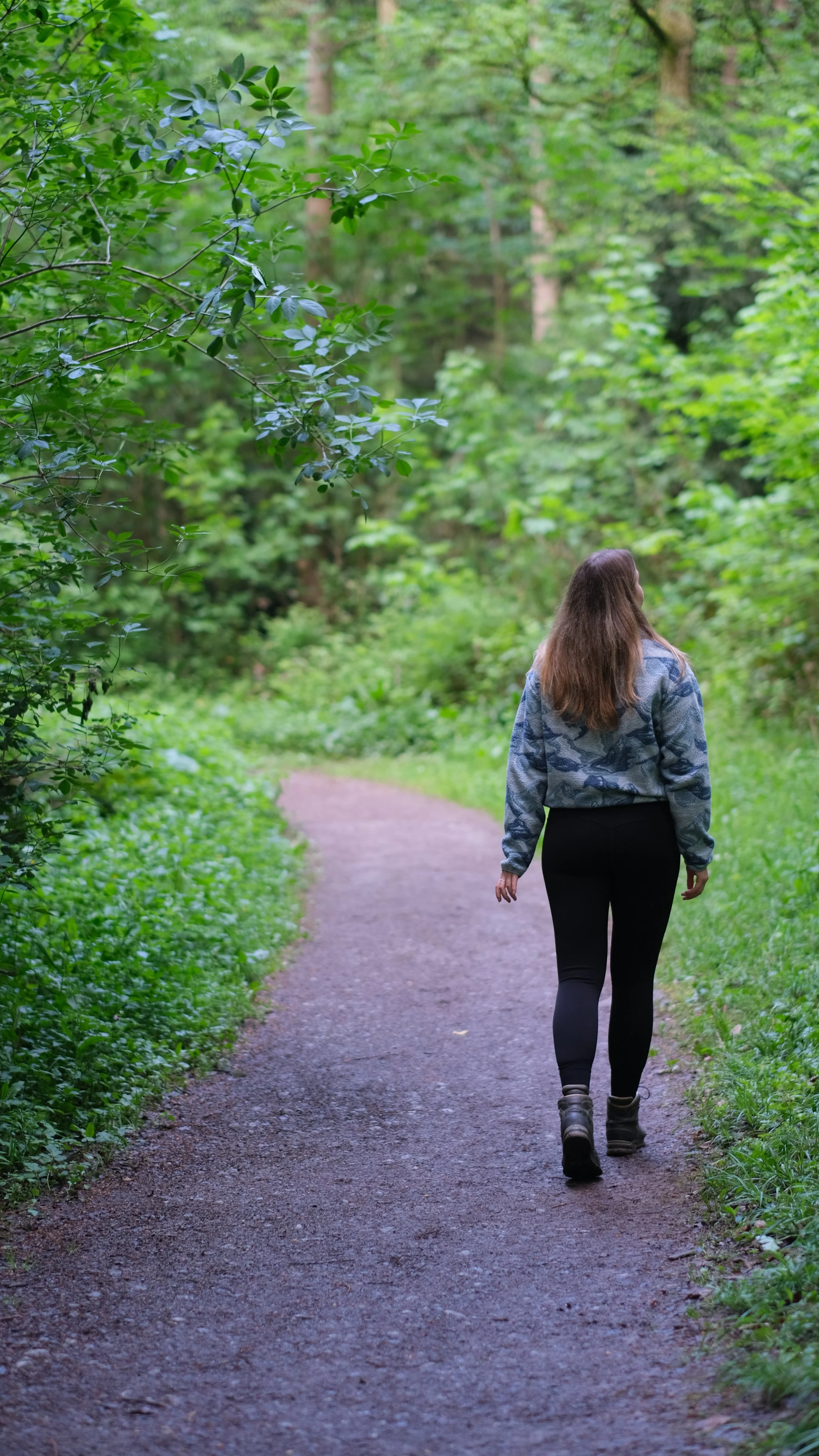 Eine Frau wandert auf einem schmalen Weg in einem grünen, bewaldeten Gebiet.