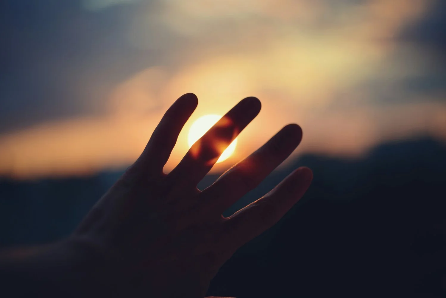 Silhouetted hand reaching toward a glowing sunset, evoking spiritual longing and the mystic's yearning for the Divine
