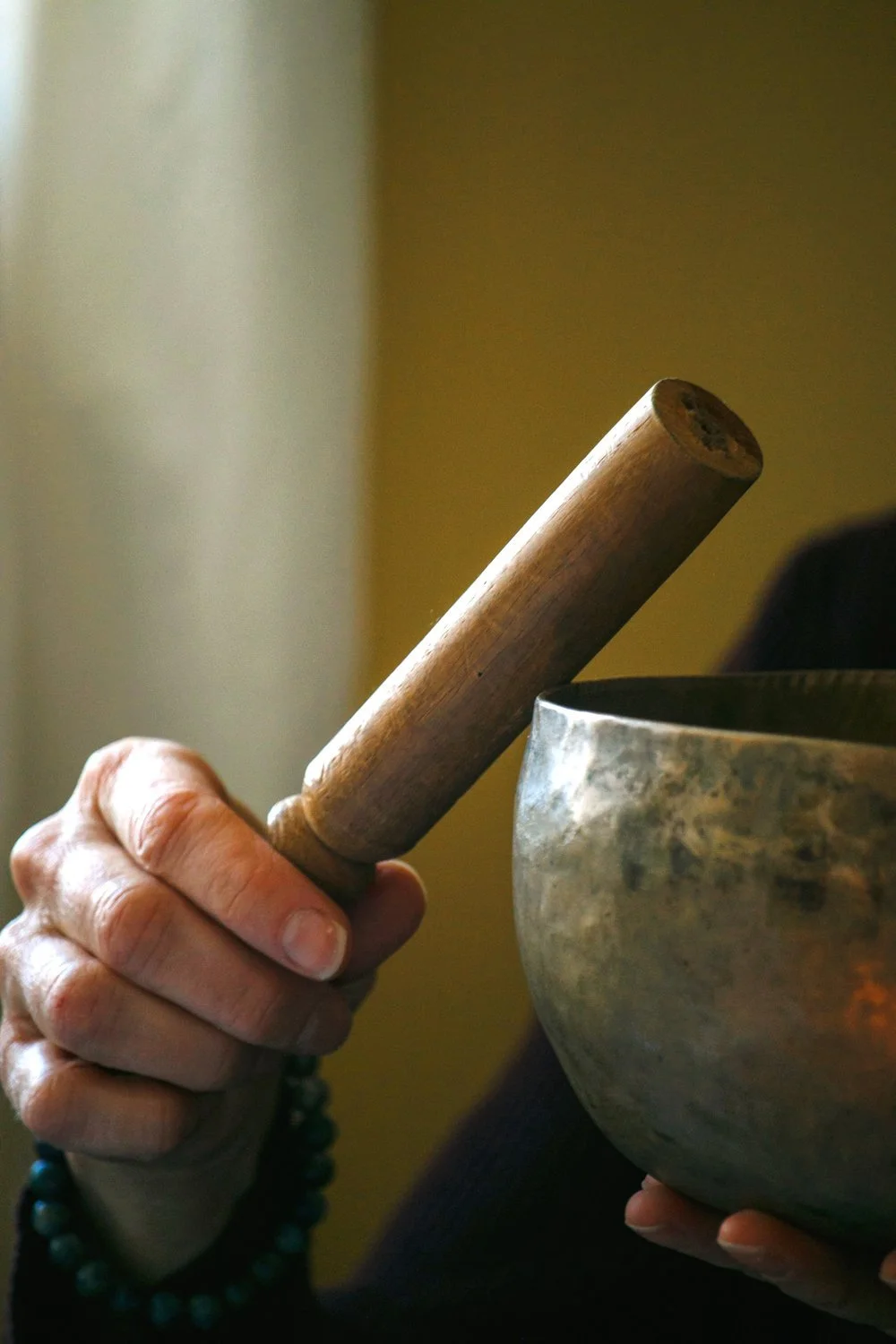 Hands holding a wooden mallet and a bronze Tibetan singing bowl, representing meditation, sound practice and centring