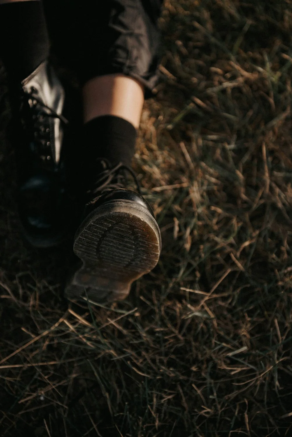 Overhead view of booted legs resting in sunlit grass, representing grounded presence and Eco Ministry's rootedness in the earth