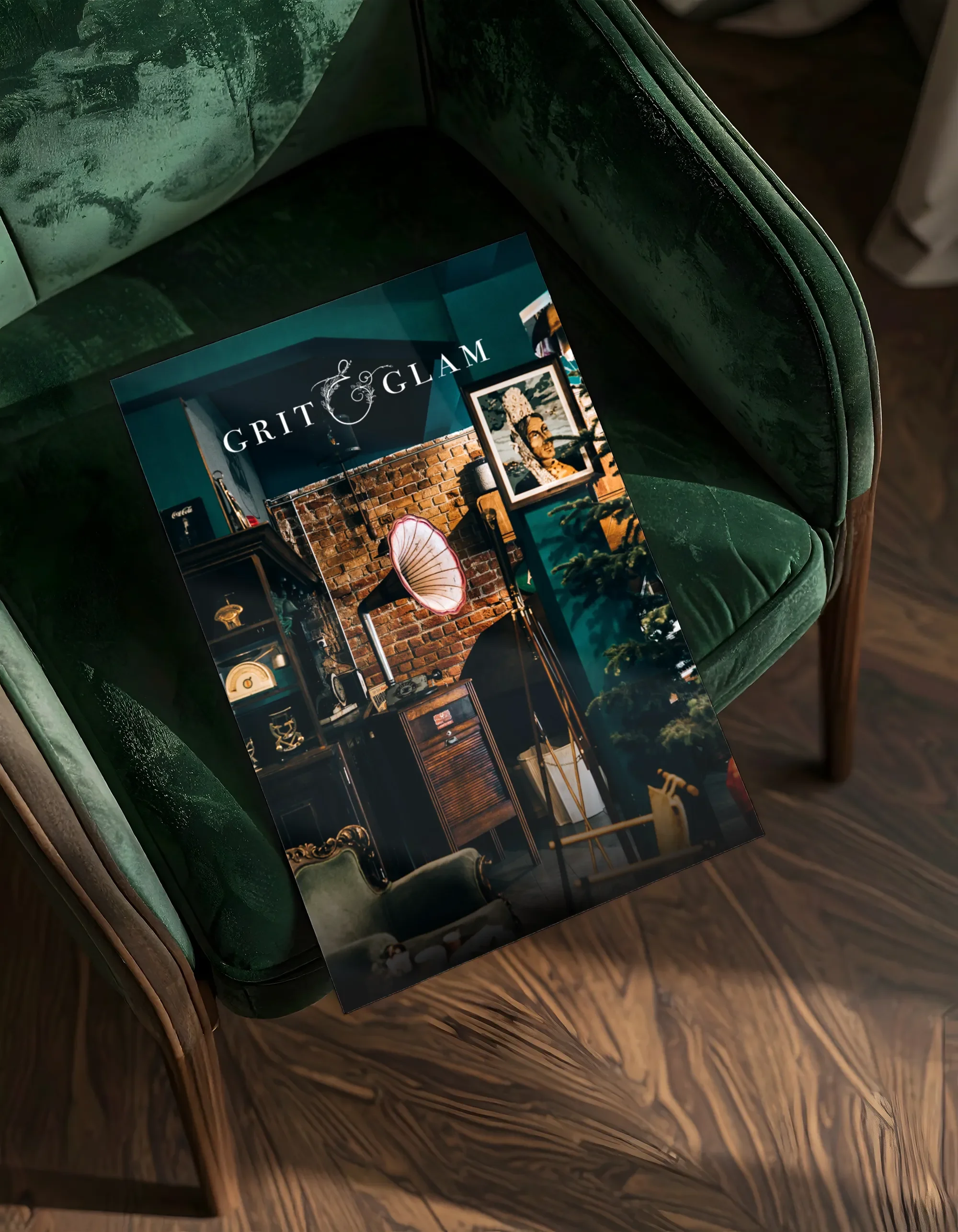 A magazine titled 'Grit & Glam' resting on a green velvet armchair. The magazine features interior decor with brick walls, antique furniture, and decorative items.
