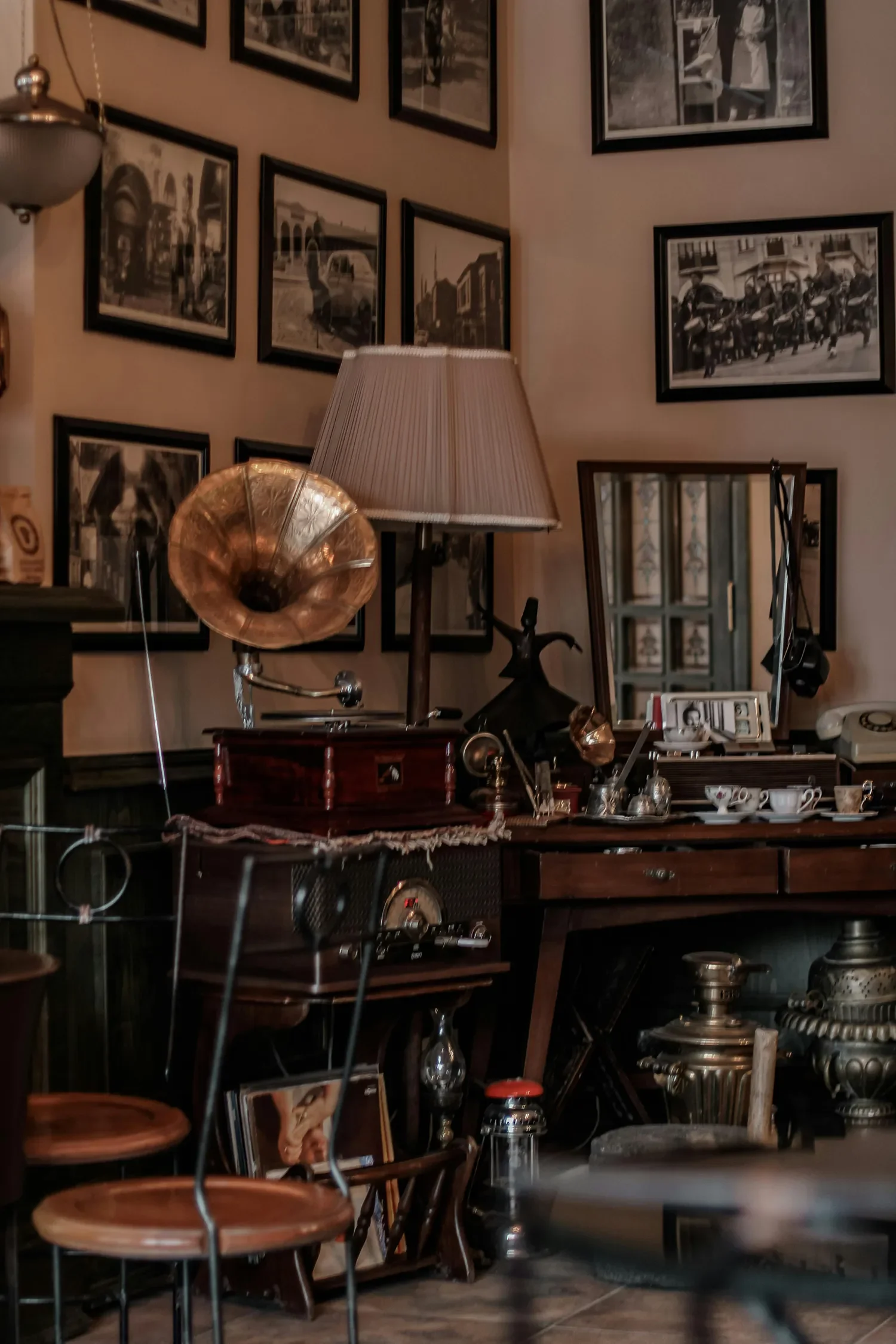 Interior of a vintage-style room with framed black-and-white photographs on the wall, a vintage gramophone, a table with cups and saucers, and various antique items.