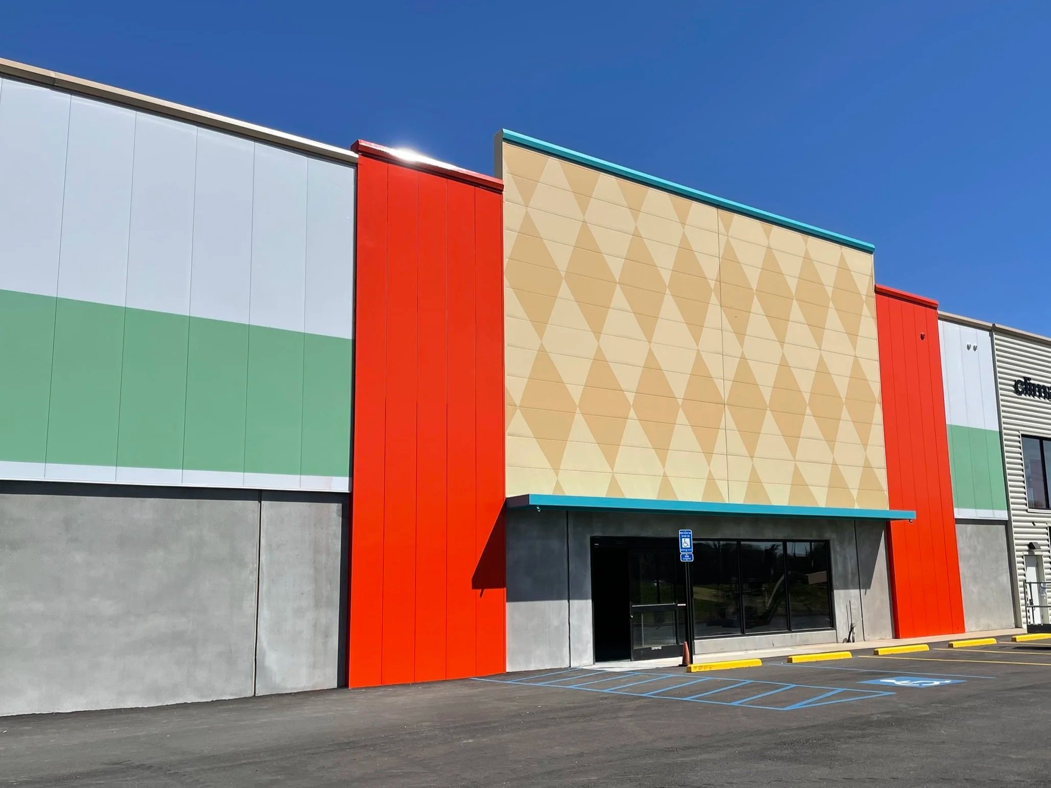 The exterior of a modern retail store with colorful geometric design panels in red, beige, green, and white, under a clear blue sky.