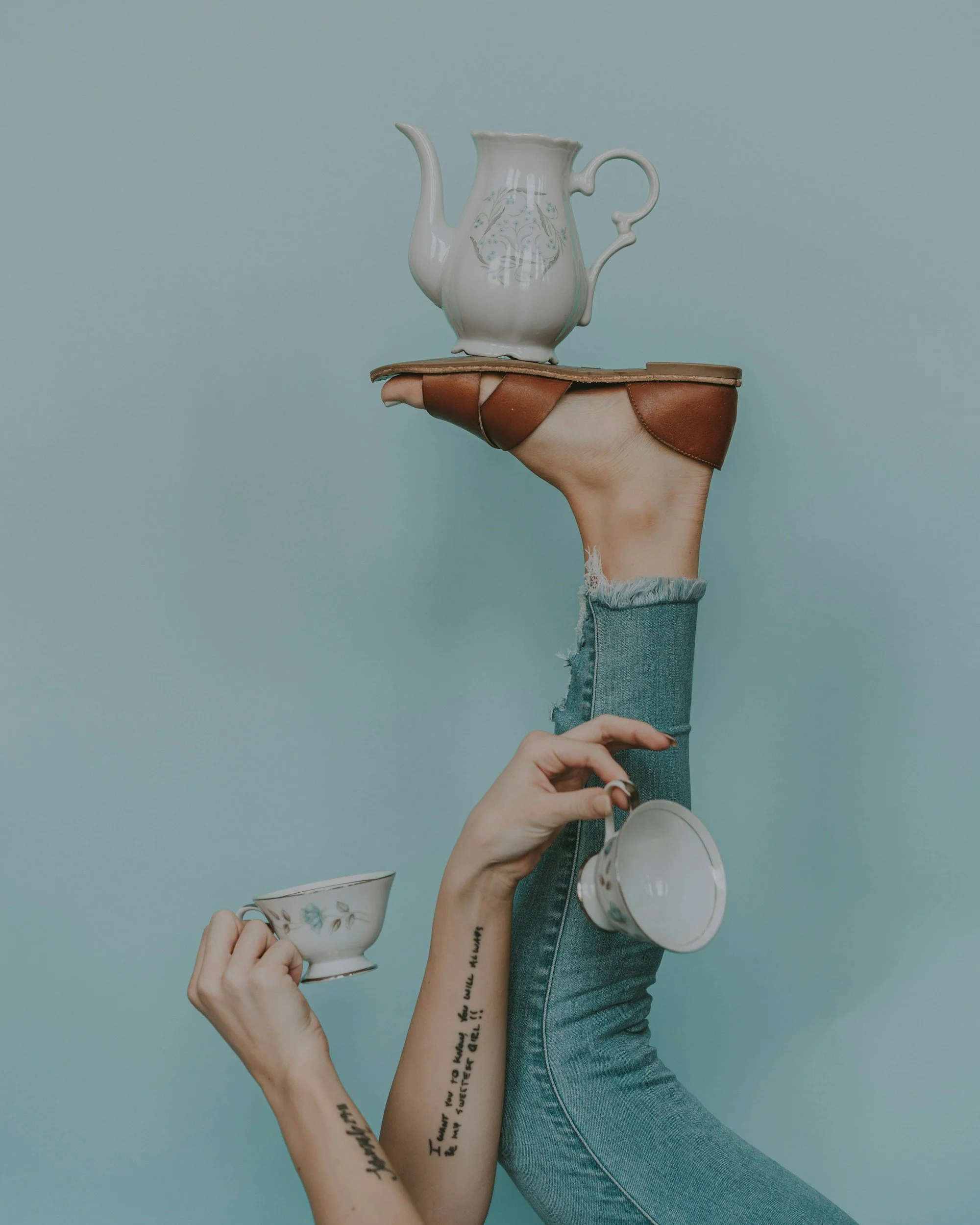 Photograph of woman balancing teapot on foot and holding dainty tea cups