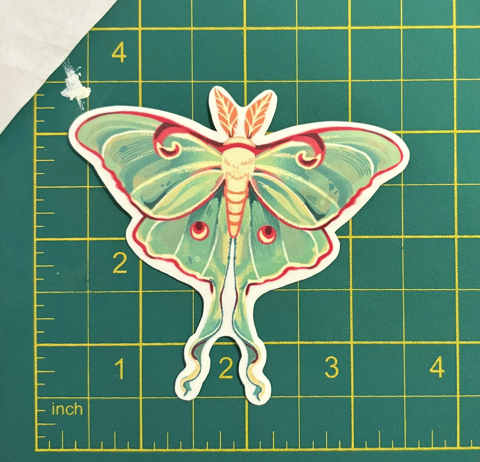 Colorful butterfly sticker with green, yellow, and red details on a green cutting mat with yellow grid lines.