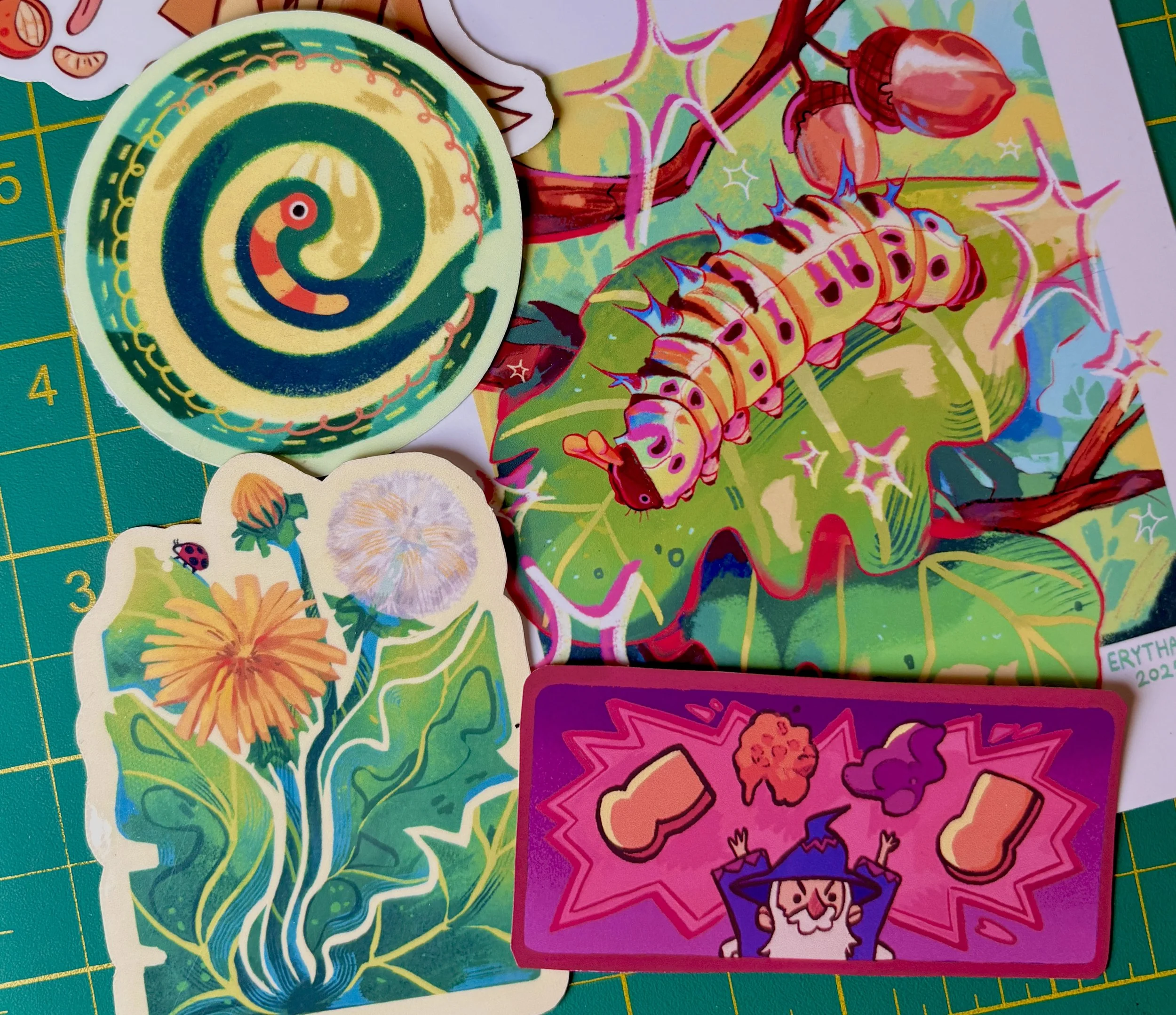 Colorful stickers with various designs, including a spiral pattern, a caterpillar, and abstract floral shapes on a green cutting mat.