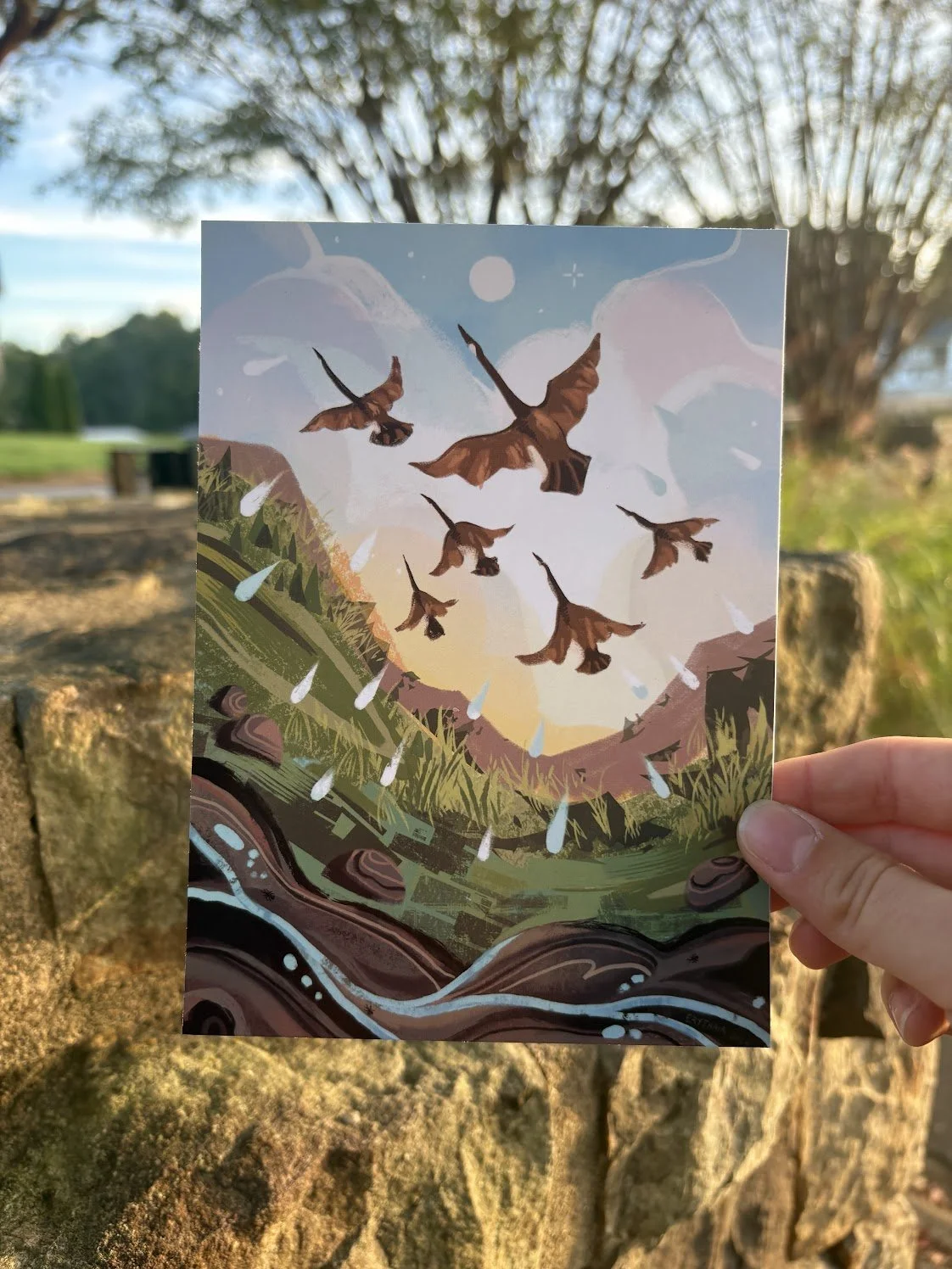 Illustration of birds flying over a landscape with hills, mountains, and a river at sunset or sunrise.