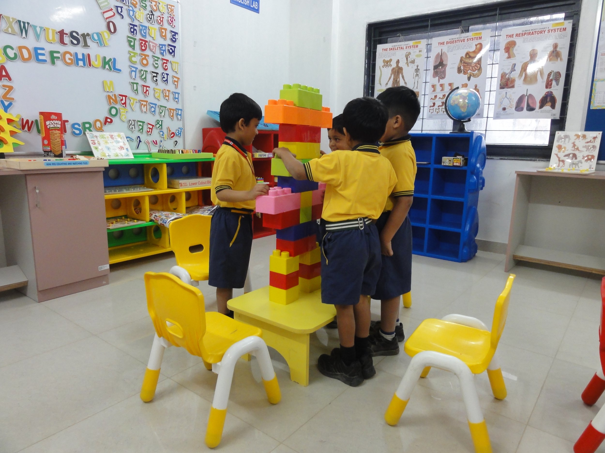 Children in yellow school uniforms playing with large colorful building blocks in a classroom.