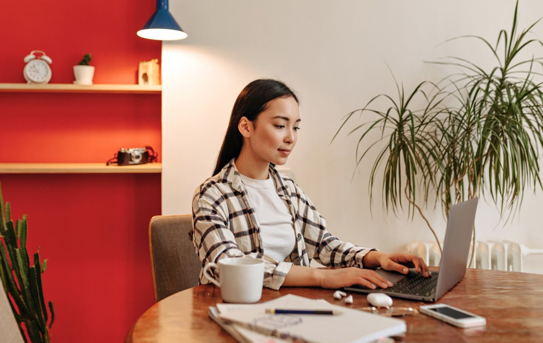 A professional woman working on a laptop at a desk with a warm coffee mug and indoor plant, illustrating a guide to optimizing LinkedIn presence.