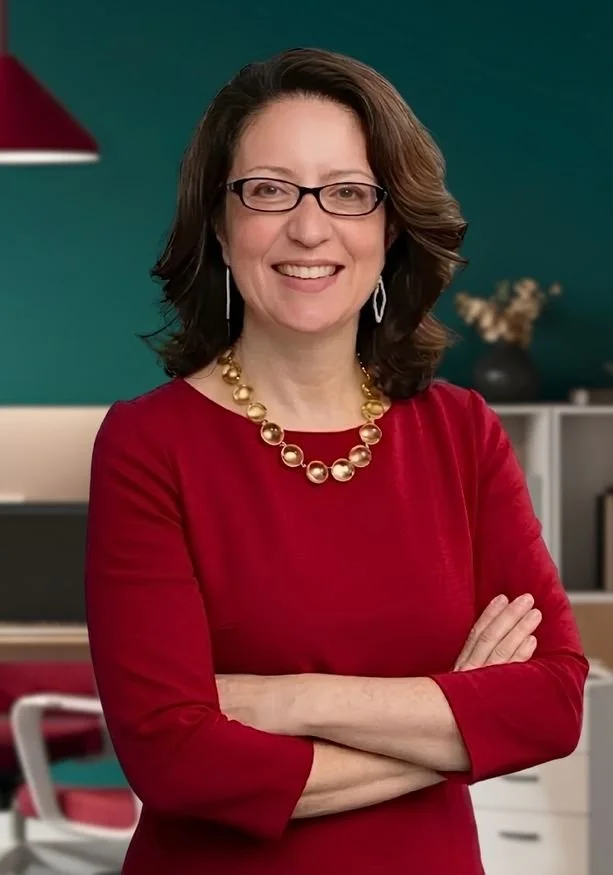 Wendy Maldonado wearing glasses, a red dress, and a gold pearl necklace, smiling with her arms crossed, standing in an office environment.