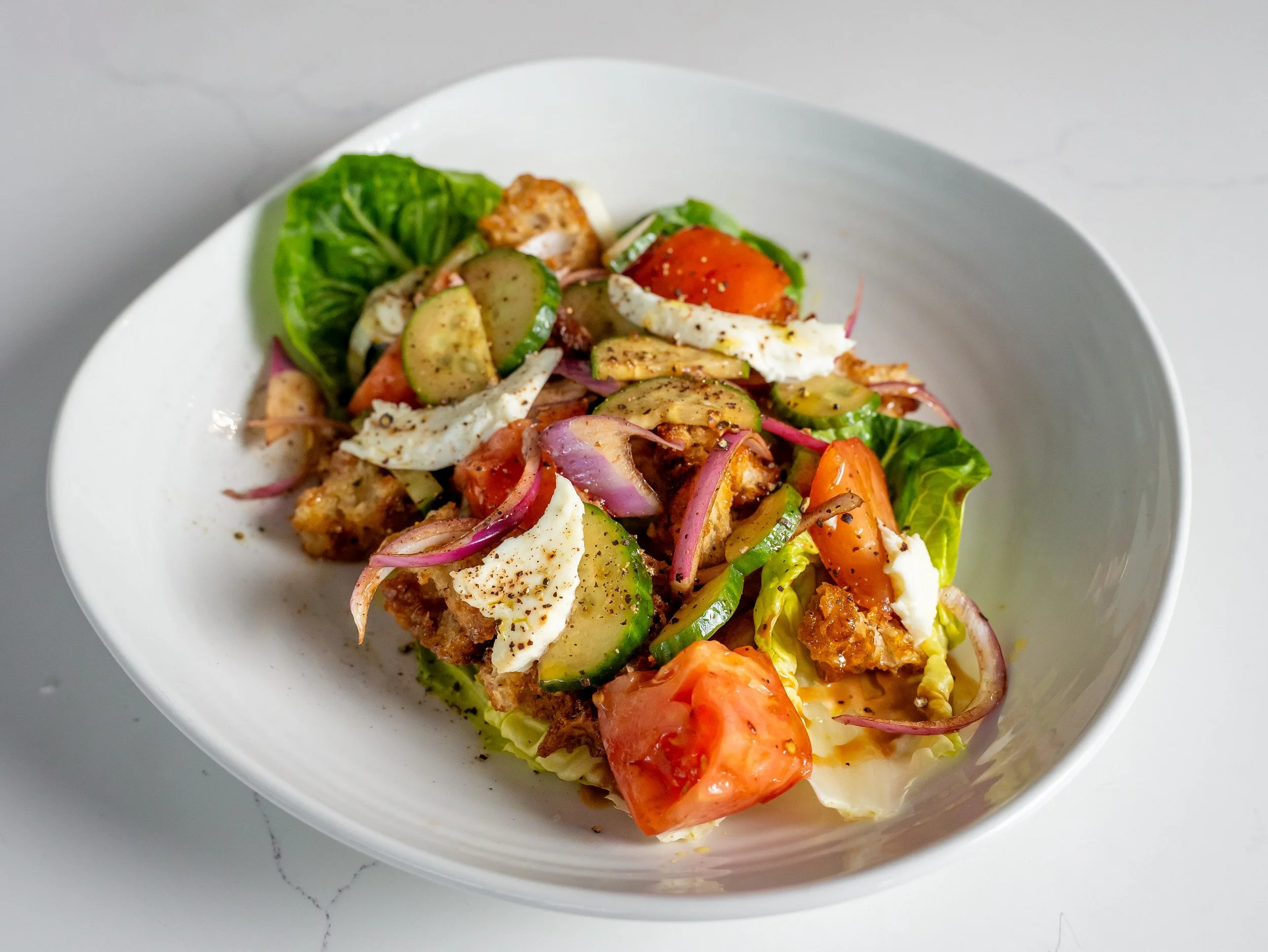 Salad with lettuce, cucumbers, tomatoes, onions, cheese, and grilled chicken in a white bowl.