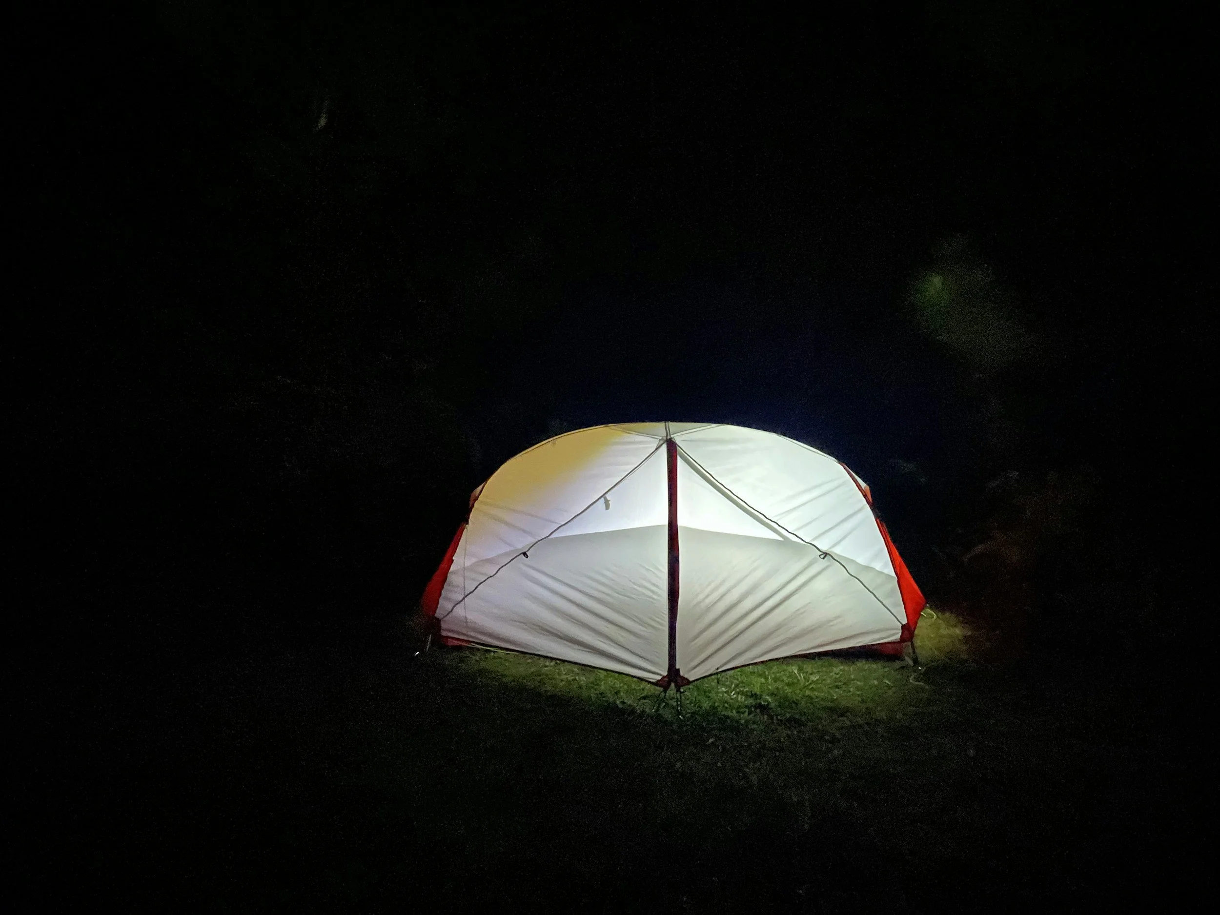 A lit umbrella on grass at night, with the moon and stars visible in the dark sky.