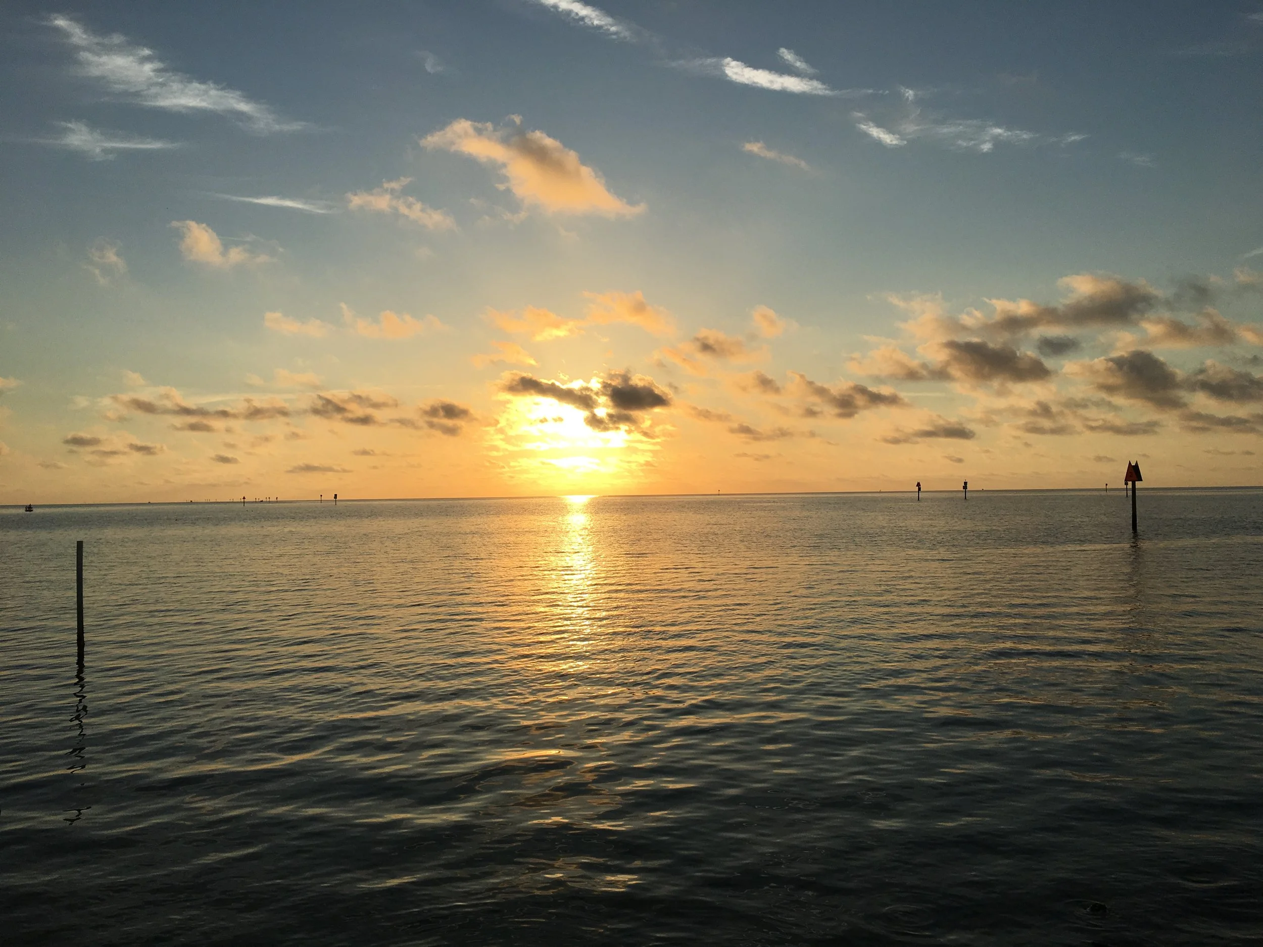 Sunset over a calm body of water with clouds in the sky and navigation markers.
