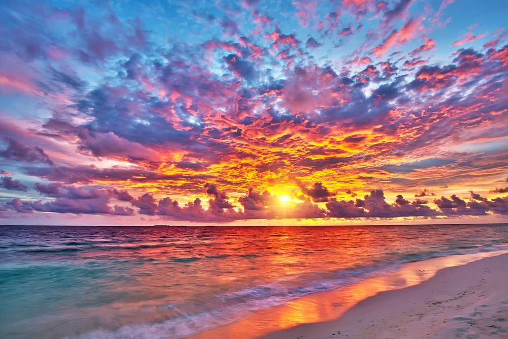 Colorful sunset over the ocean with pink, purple, and orange clouds reflecting on the water and sandy beach.