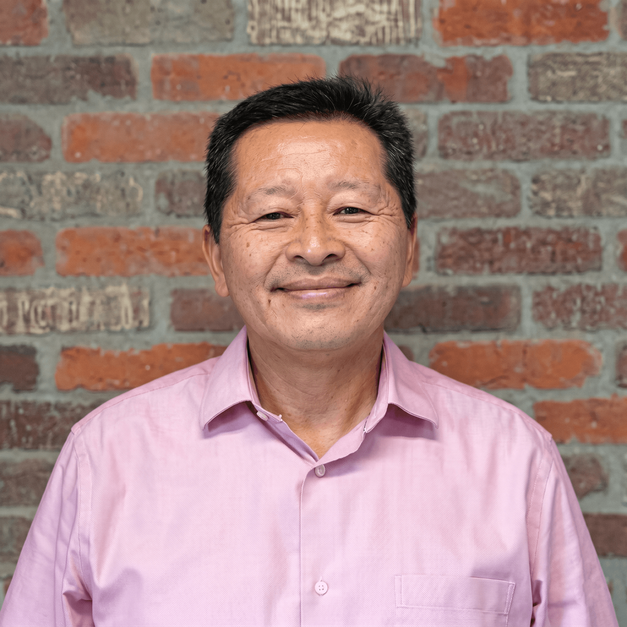 Close-up of a middle-aged Asian man smiling, wearing a pink dress shirt, standing in front of a brick wall. Hon Wong, franchise support.