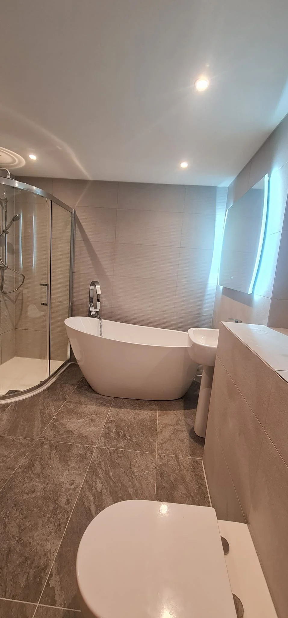 Modern bathroom with a glass shower enclosure, a freestanding bathtub, a white toilet, and a vanity with a mirror and lighting.