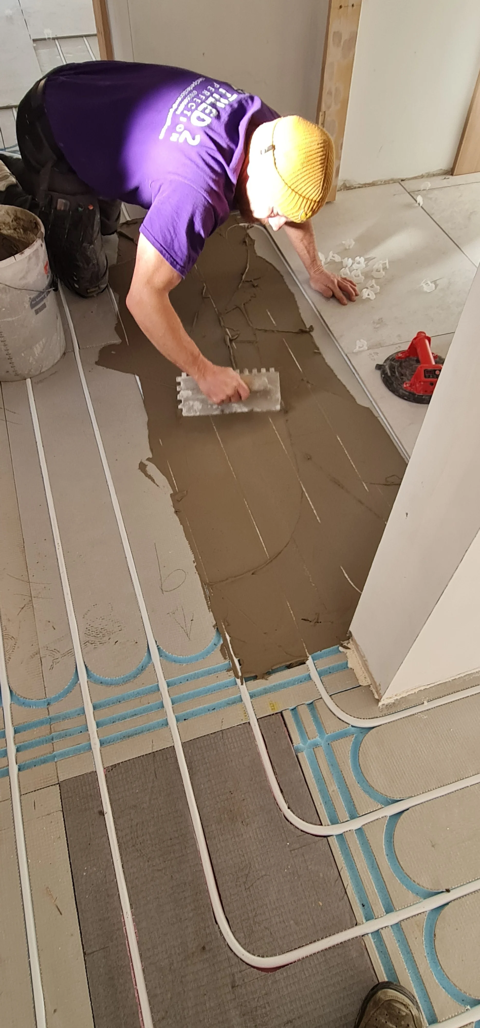 A worker installing heated floor tubing while pouring concrete to create underfloor heating.