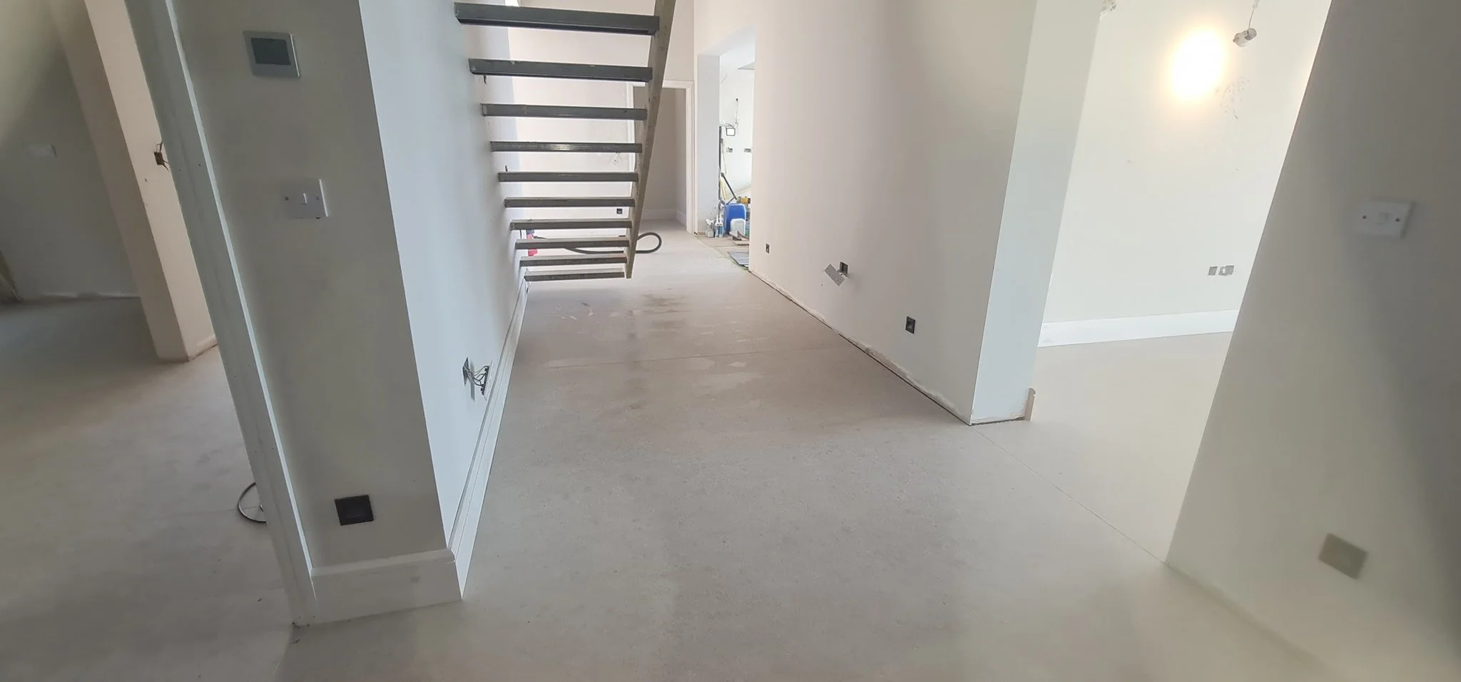 Interior of a house under construction with missing flooring, white walls, and an open staircase with black treads.