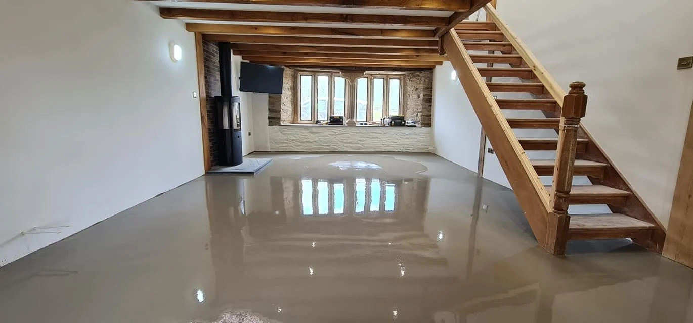 Empty living room with polished concrete floor, wooden staircase, and large windowed wall with brick accents.