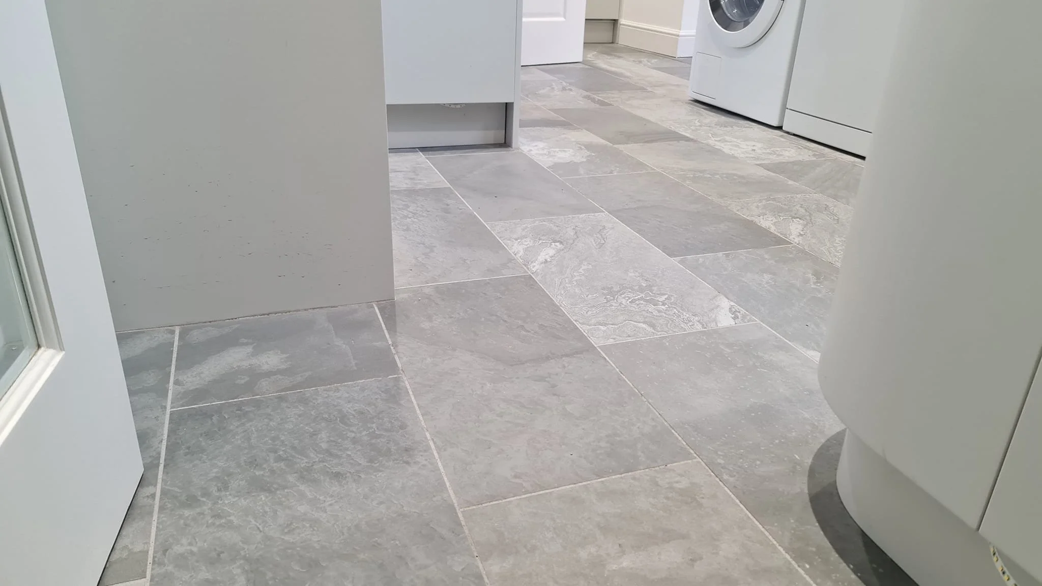 Laundry room with gray tiled floor, front of a white washing machine, and a white dryer, with white walls and baseboards.