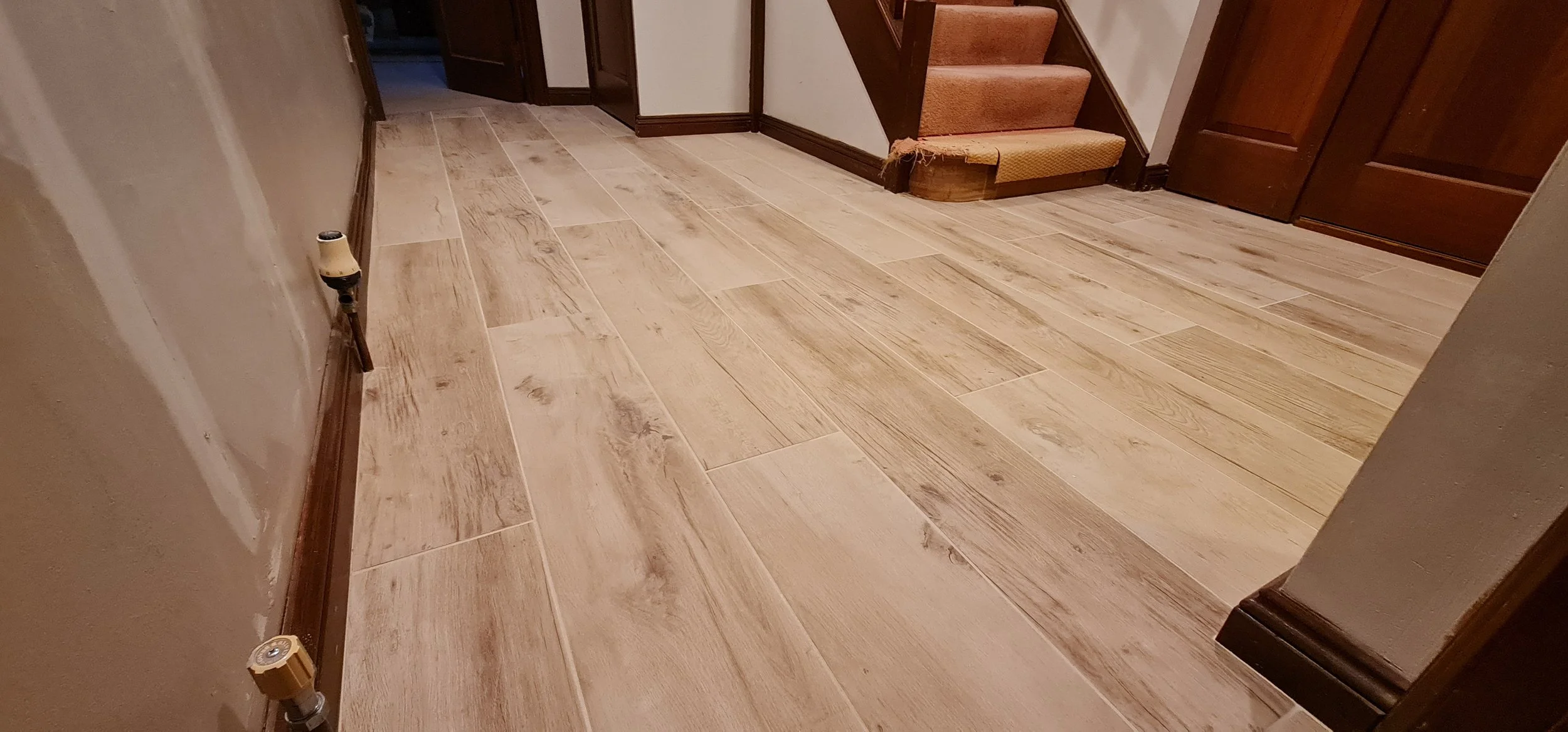 A hallway with wood-look tile flooring, baseboards, and a staircase with carpeted steps at the end.