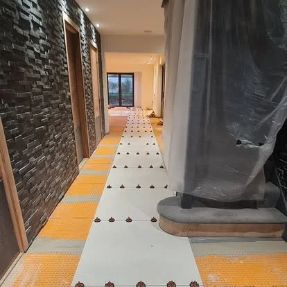 Hallway under construction with protective coverings, construction materials, and partially installed flooring.