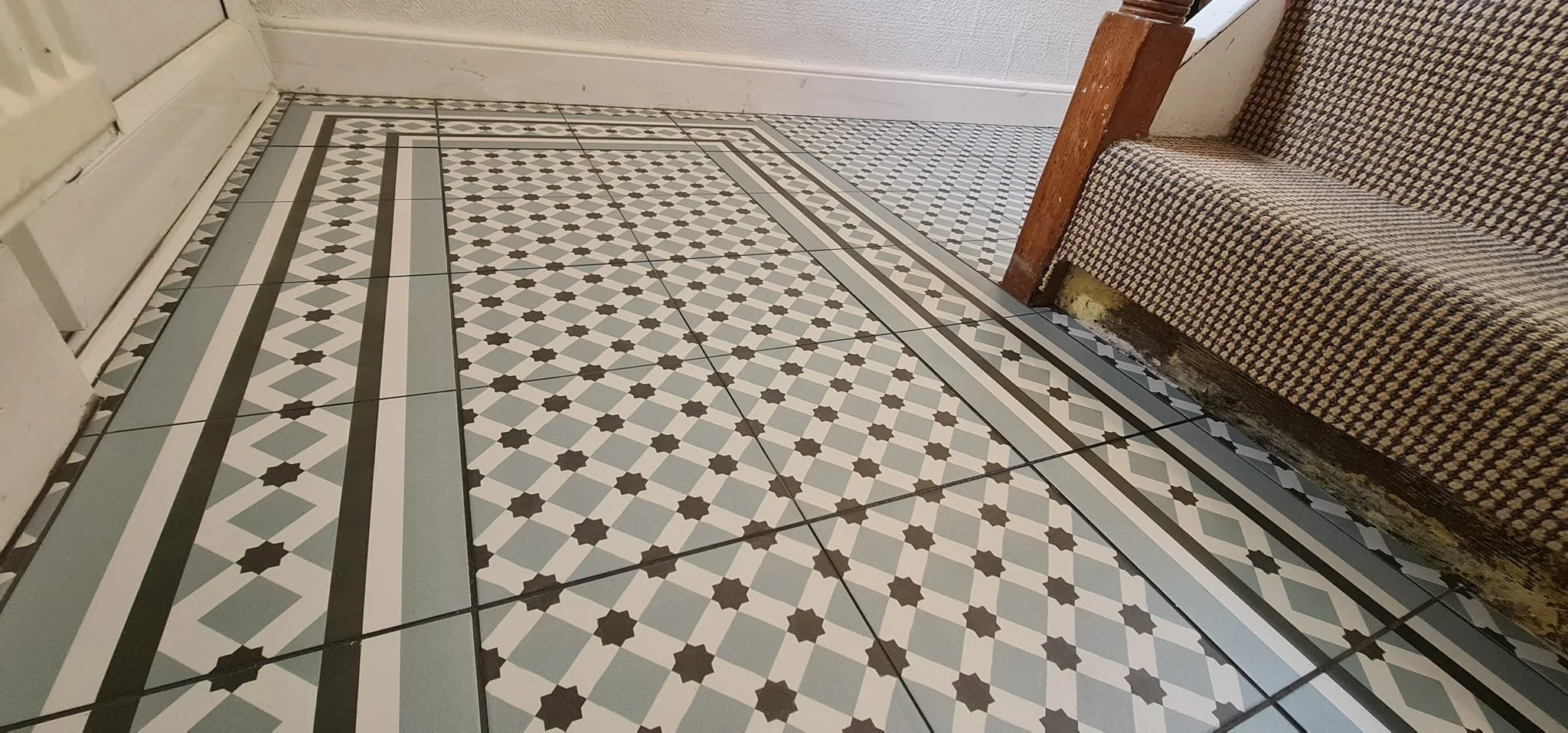 Close-up of a patterned tiled floor next to a wooden bench and a white wall.