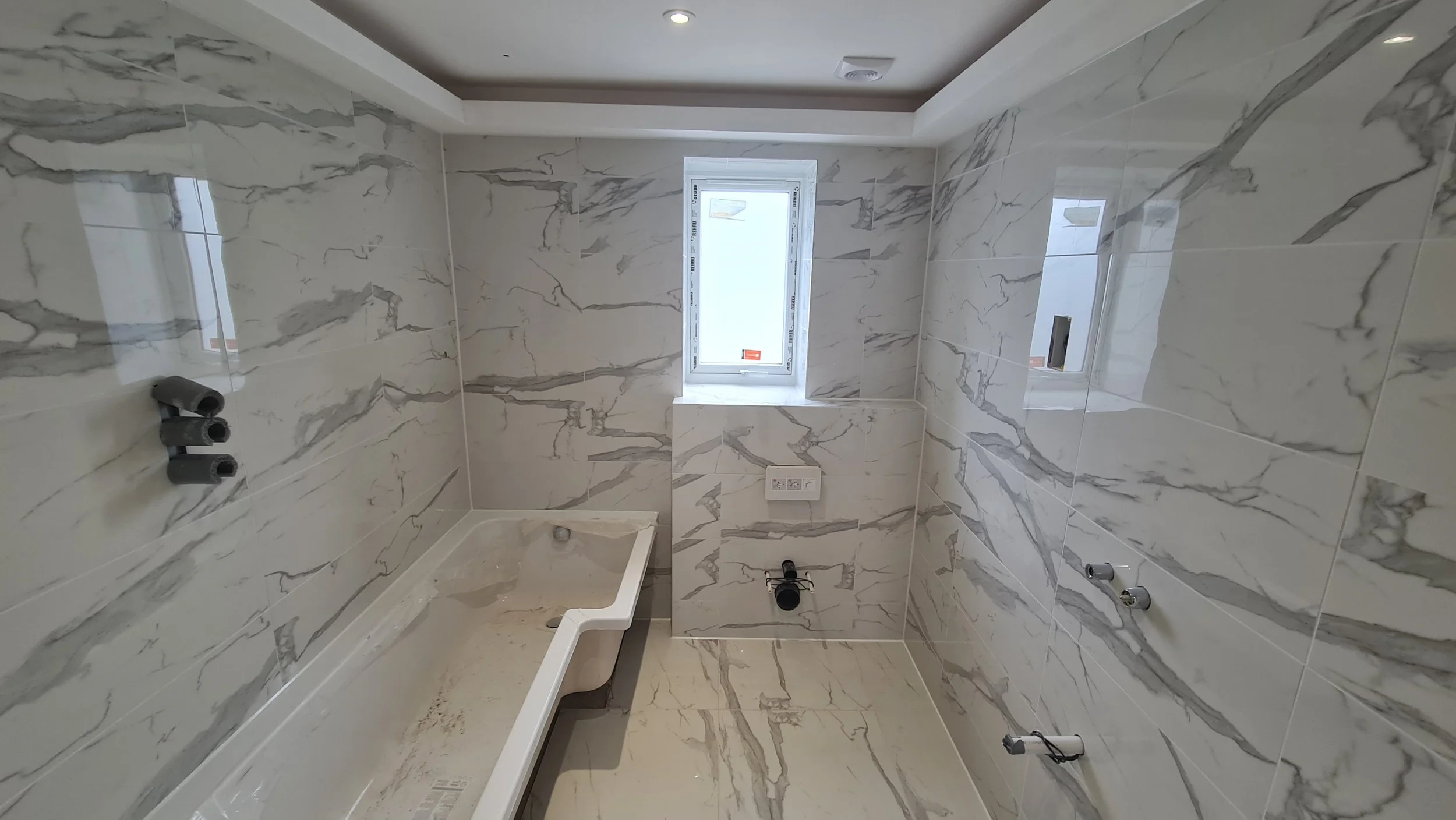 Bathroom with marble tiles, a small frosted window, and plumbing fixtures for a sink and toilet.