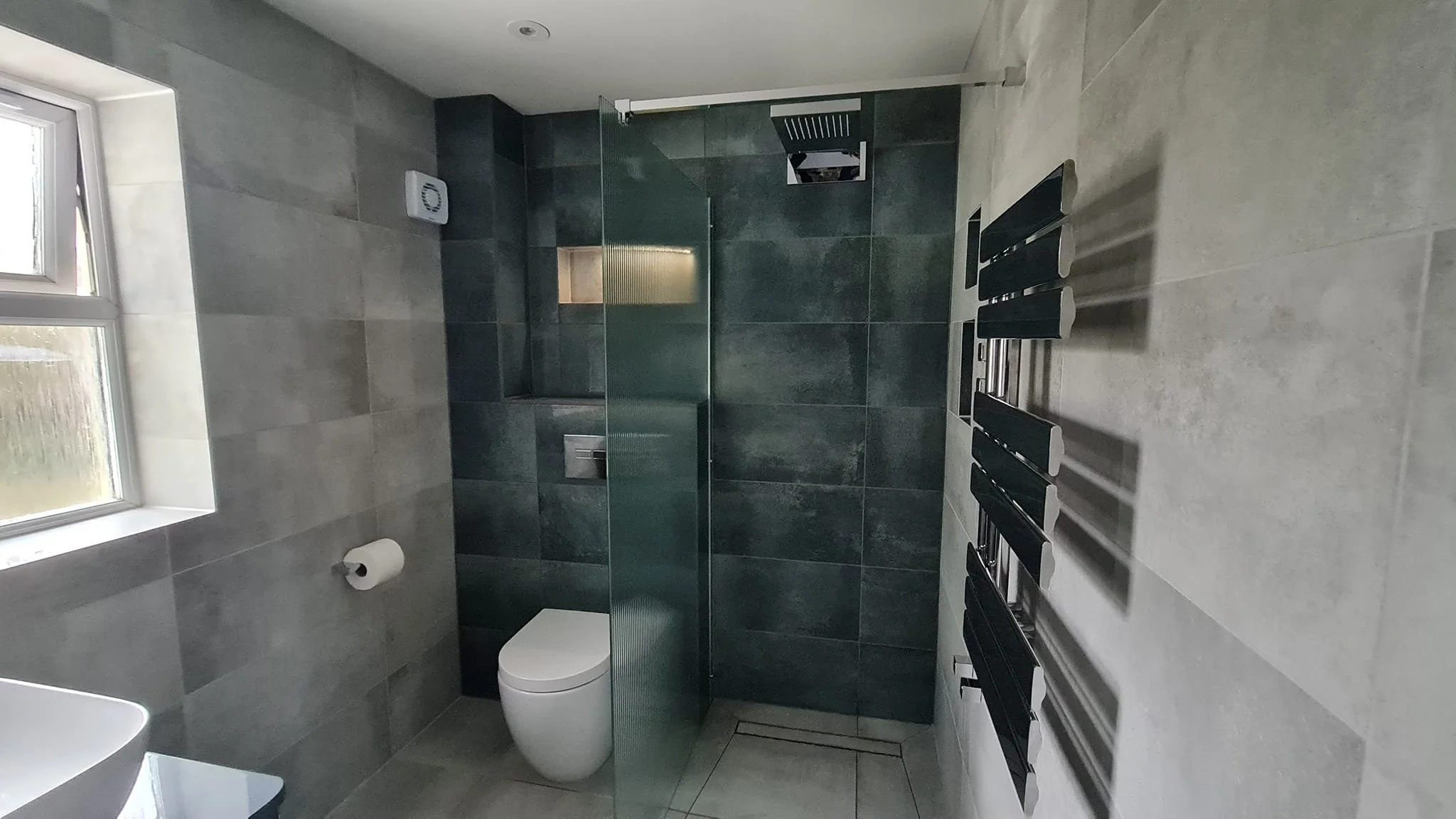 Modern bathroom with gray tiles, glass shower enclosure, white toilet, and a heated towel rail on the wall.