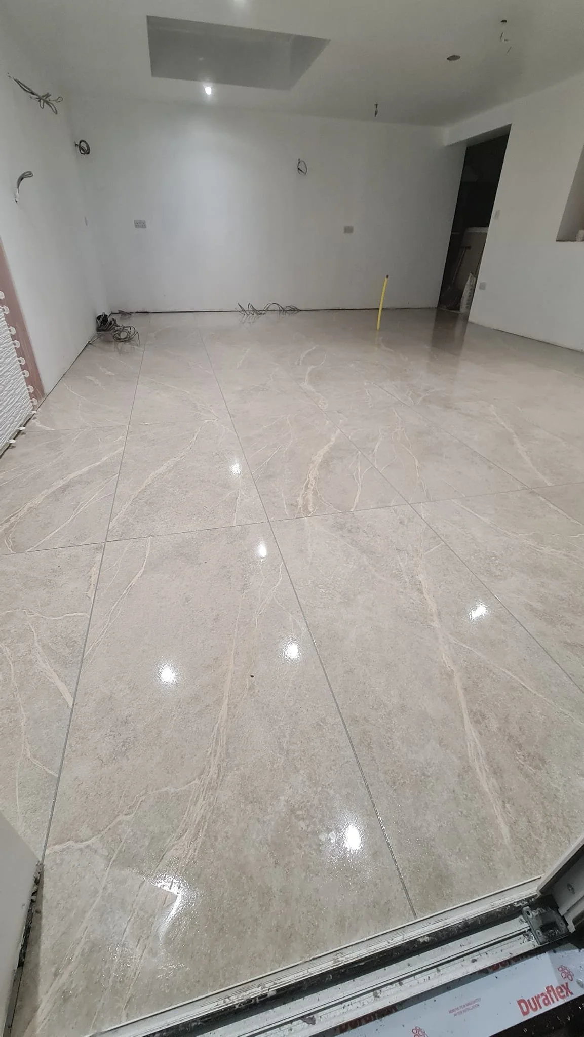 Interior room with freshly installed cream-colored marble tile flooring, walls painted white, and some construction wiring visible.