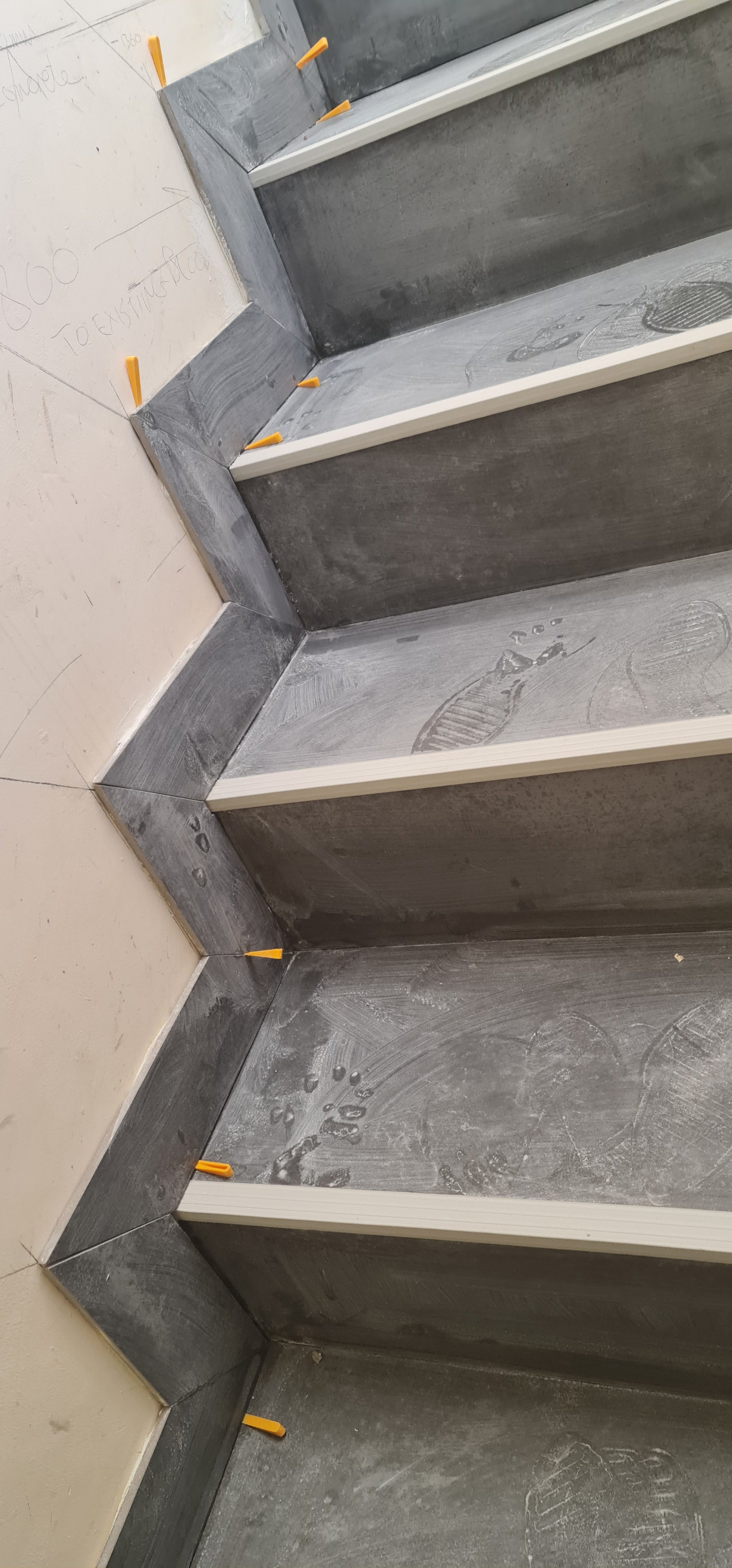 Construction of a staircase with dark treads and sides, white trim, and orange corner protectors in a building under construction.
