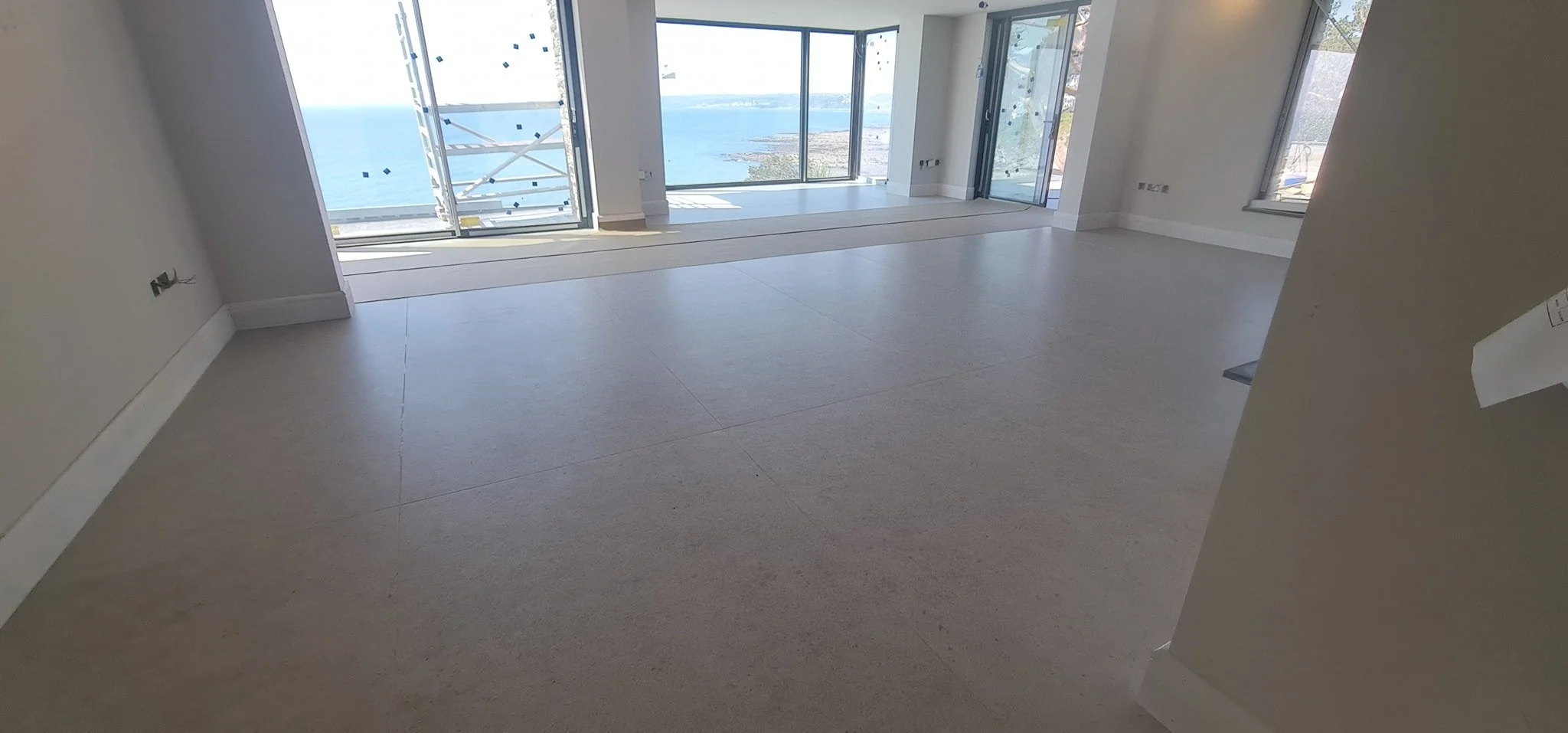 Empty room with large windows and a view of the ocean and coastline.