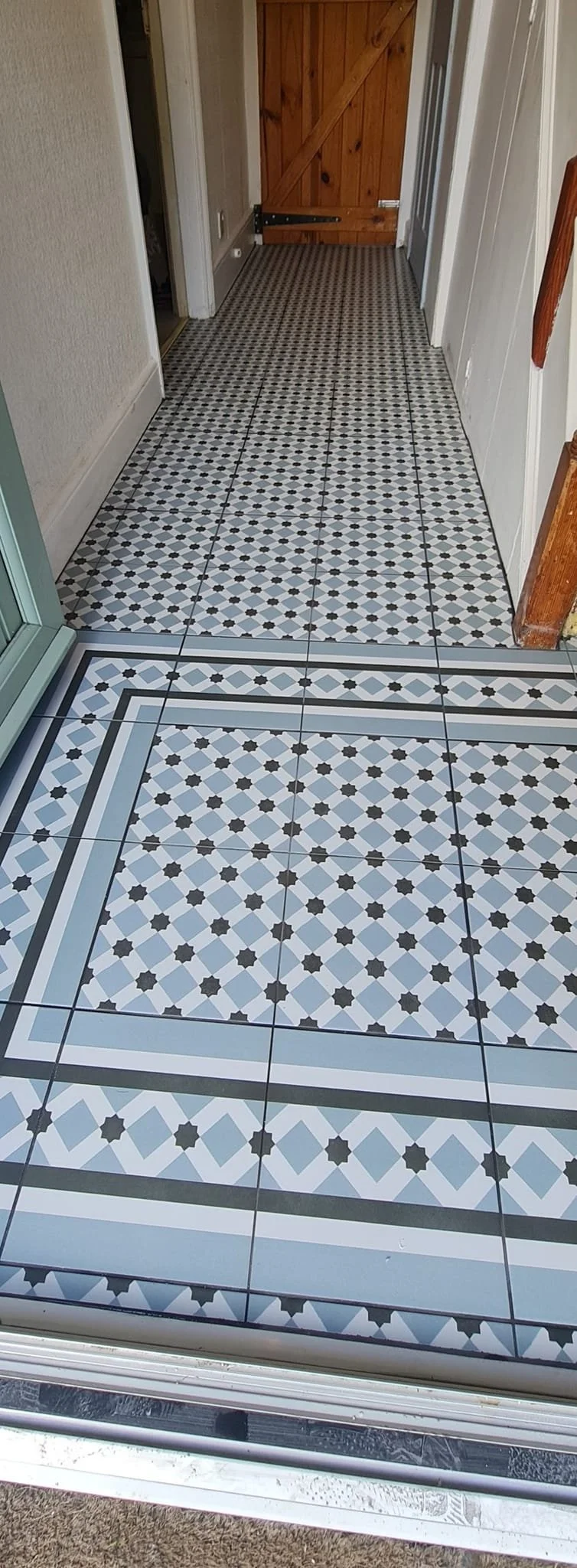 Indoor hallway with patterned tile flooring, leading to a wooden barn-style door.