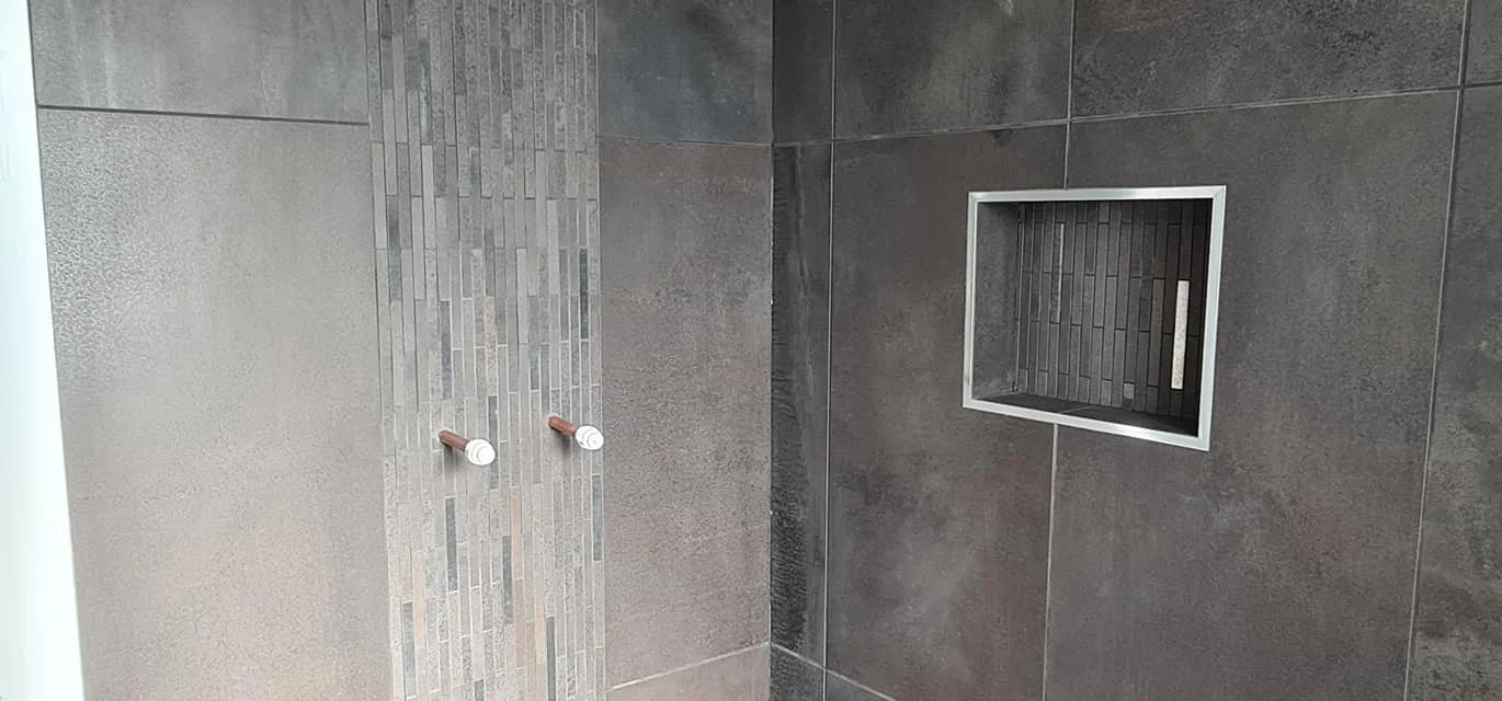 Empty shower area with dark gray tiled walls, a square shower drain, and two white showerheads.