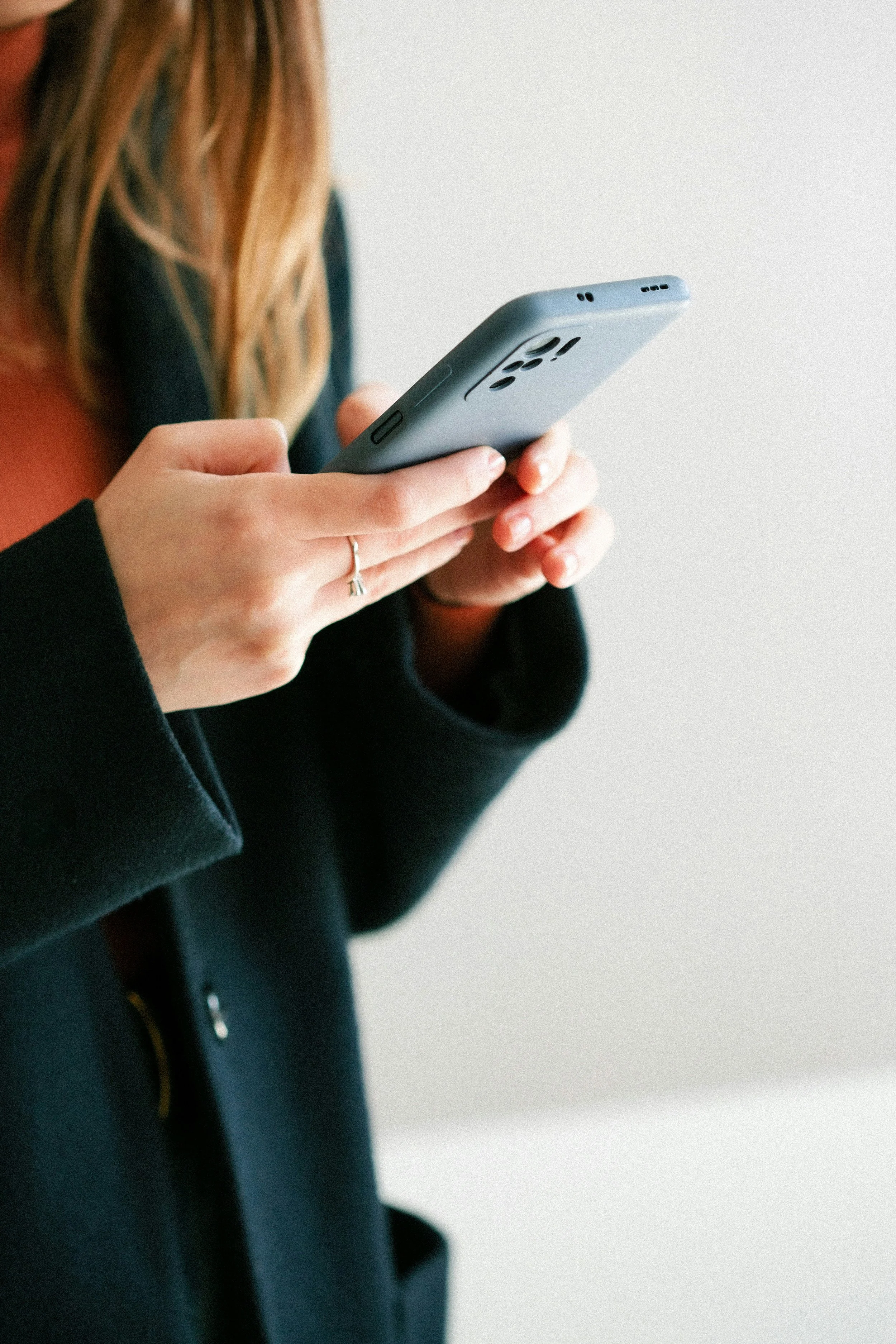 A person holding a smartphone in their hands, wearing a black jacket and a ring on their finger.