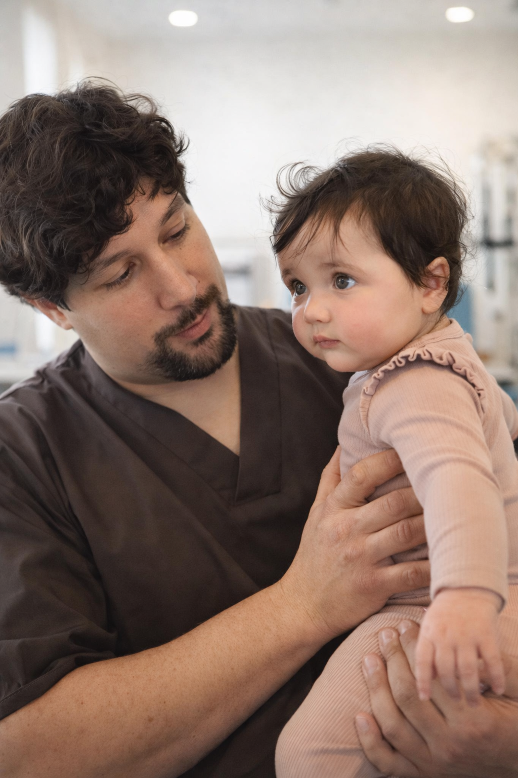 A man, likely a healthcare worker, holding a young girl in a clinical setting.