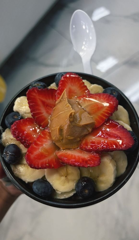 A bowl of sliced strawberries, bananas, blueberries, topped with peanut butter and honey.