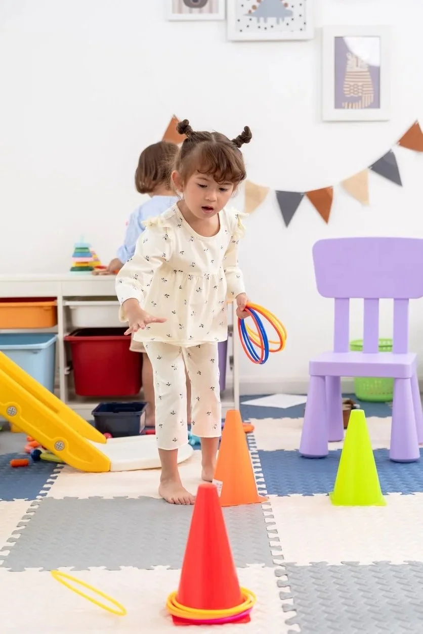 Young girl participating in an obstacle course involving colorful cones and rings during play-based speech therapy for kids in Waterford, WI.