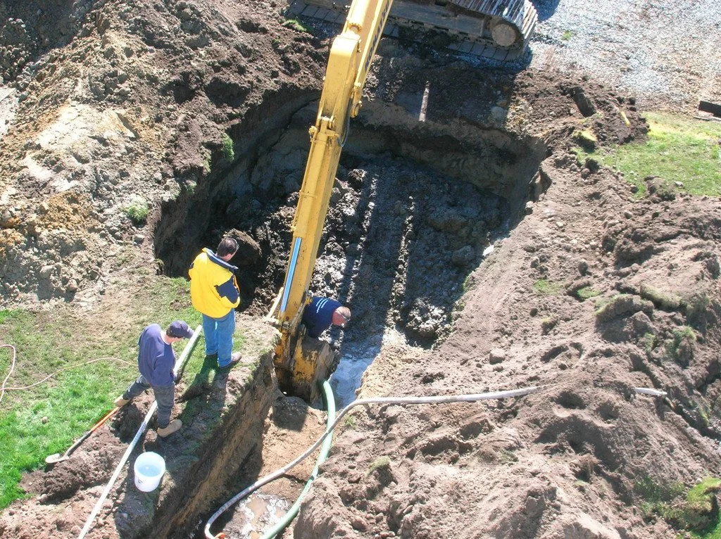 Three workers in a trench with a yellow excavator digging deep into the ground, septic design , installation and repair south county