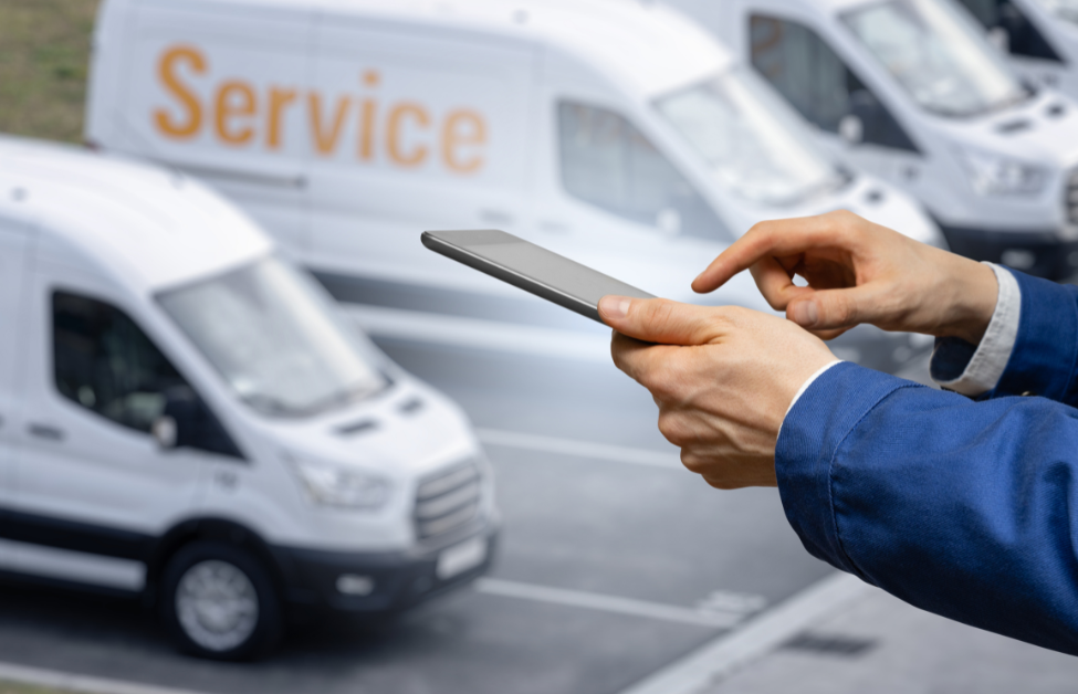 Persona usando un teléfono móvil frente a una fila de camionetas blancas, una con la palabra 'Service' en la puerta