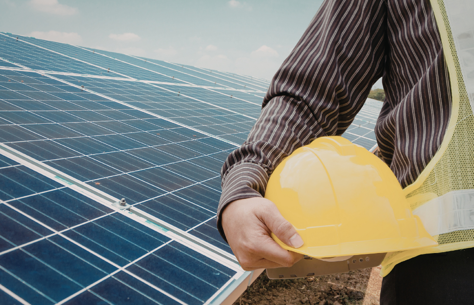 Persona con casco y chaleco de seguridad en un campo de paneles solares.