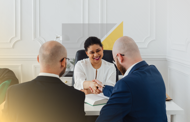 Mujer sonriendo y estrechando manos en una oficina con dos hombres sorprendidos.